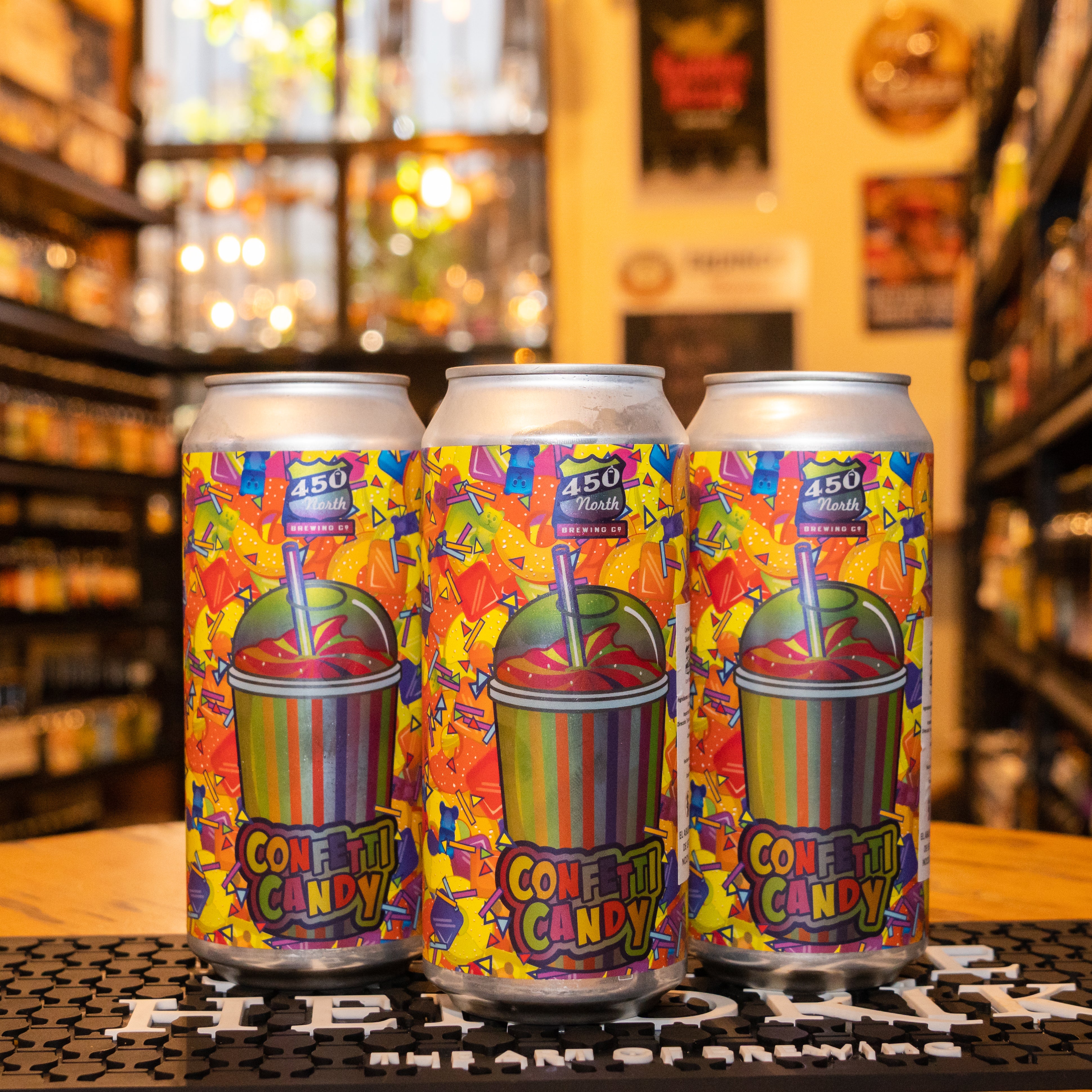 Botella de 450 North Confetti Candy, una cerveza de edición especial estilo Slushy Fruited Sour de 450 North Brewing Company. La etiqueta es colorida y vibrante, con un diseño inspirado en caramelos y frutas tropicales. ABV de aproximadamente 6%, con un aroma dulce y frutal, y sabores de frutas mezcladas con un toque ácido. Ideal para disfrutar sola o acompañar platos ligeros y frescos. El diseño refleja un estilo extravagante y frutal.