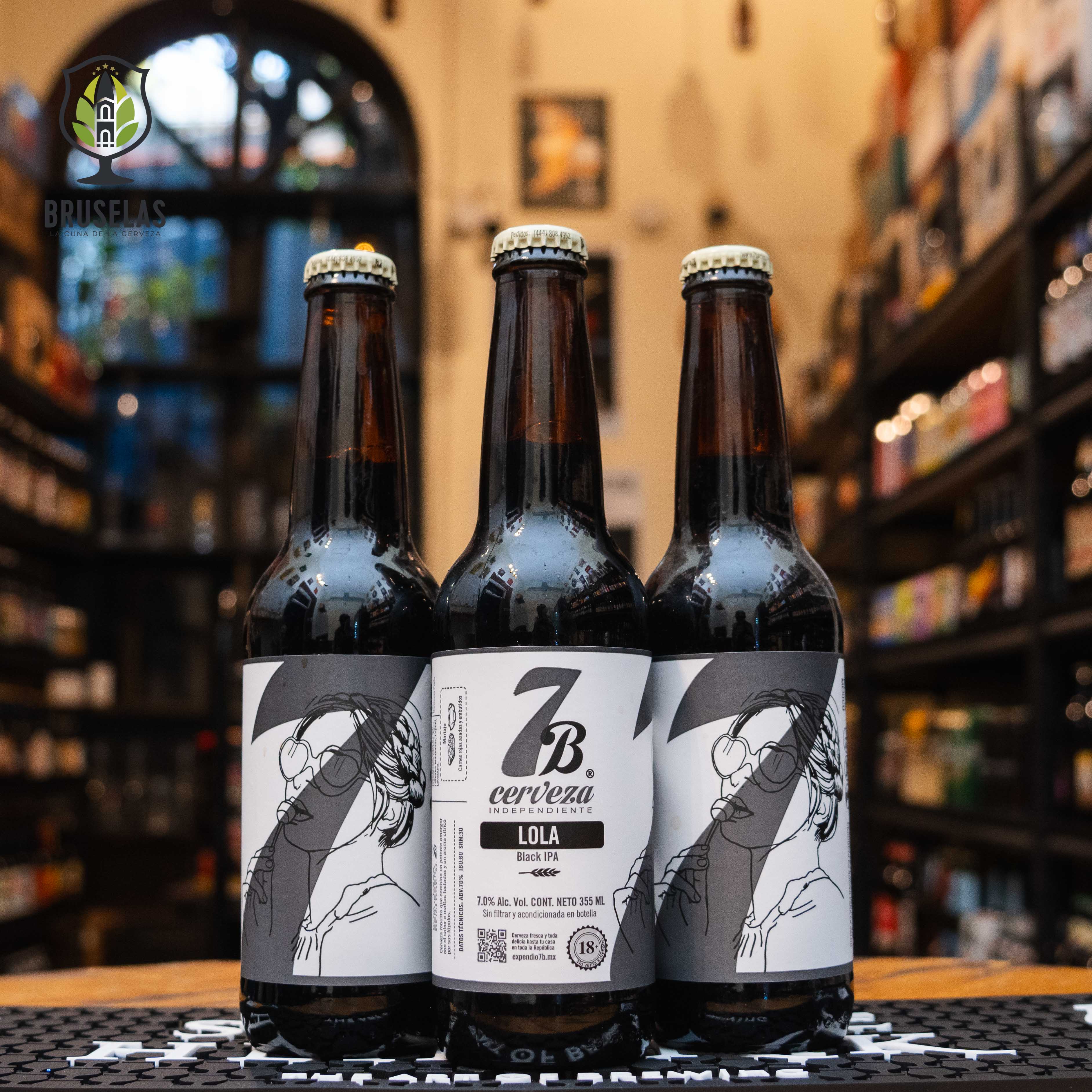 Botella de 7 Barrios Lola, una Black IPA artesanal de Cervecería 7 Barrios en San Luis Potosí. La etiqueta es blanca y negra con una ilustración de una mujer. ABV de 7.0%, con un potente amargor, maltas tostadas y un aroma cítrico de lúpulo. Ideal para maridar con carnes rojas asadas y embutidos. El diseño refleja el carácter robusto y artesanal de esta cerveza.