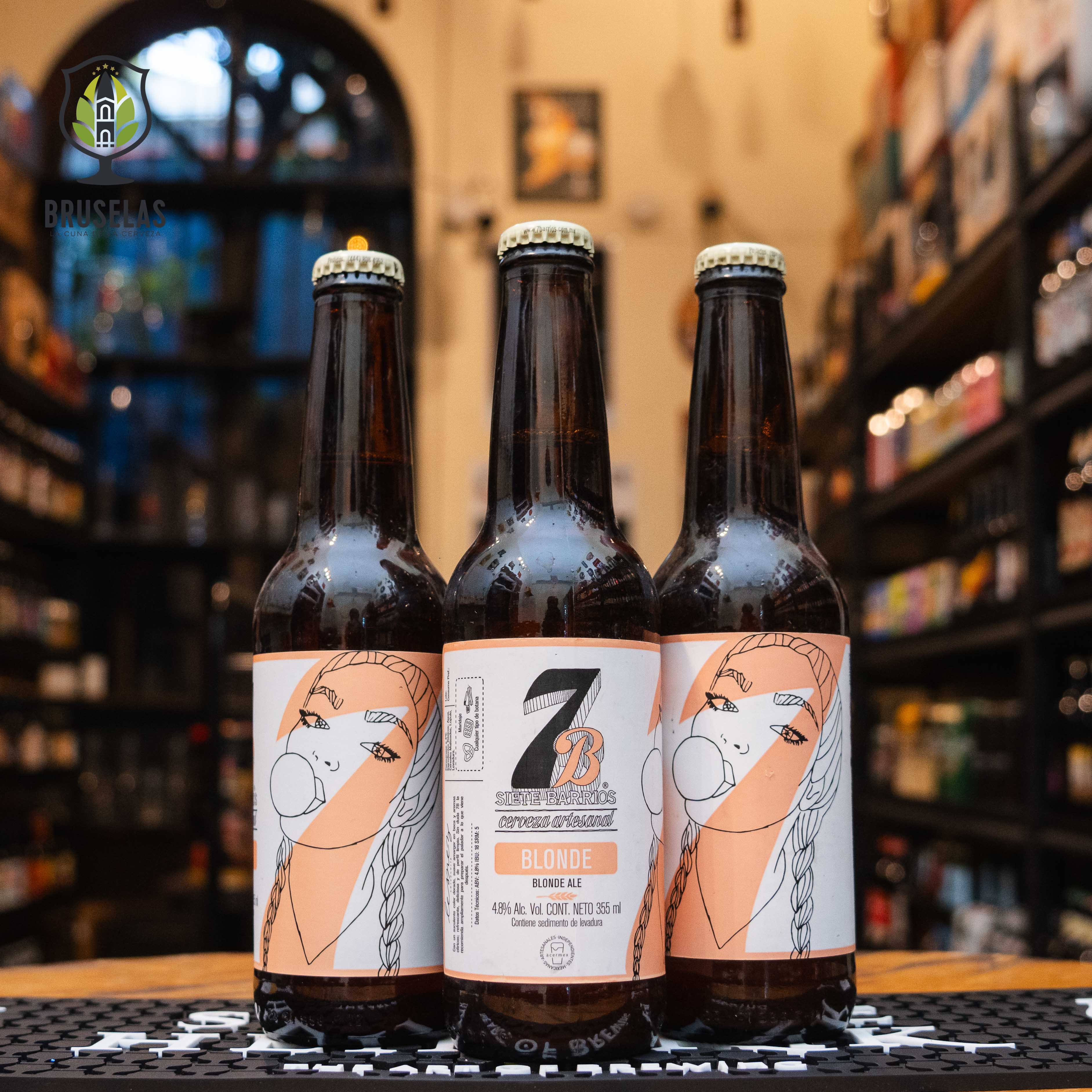 Botella de 7 Barrios Blond, una Blonde Ale de Cervecería 7 Barrios, San Luis Potosí. De color amarillo dorado, su etiqueta refleja la simplicidad y elegancia de esta cerveza artesanal. ABV de 4.8%, con aroma maltoso y ligeras notas frutales. Ideal para maridar con ensaladas, pescados y mariscos. El diseño de la botella resalta su carácter suave y equilibrado, perfecta para una tarde relajada.