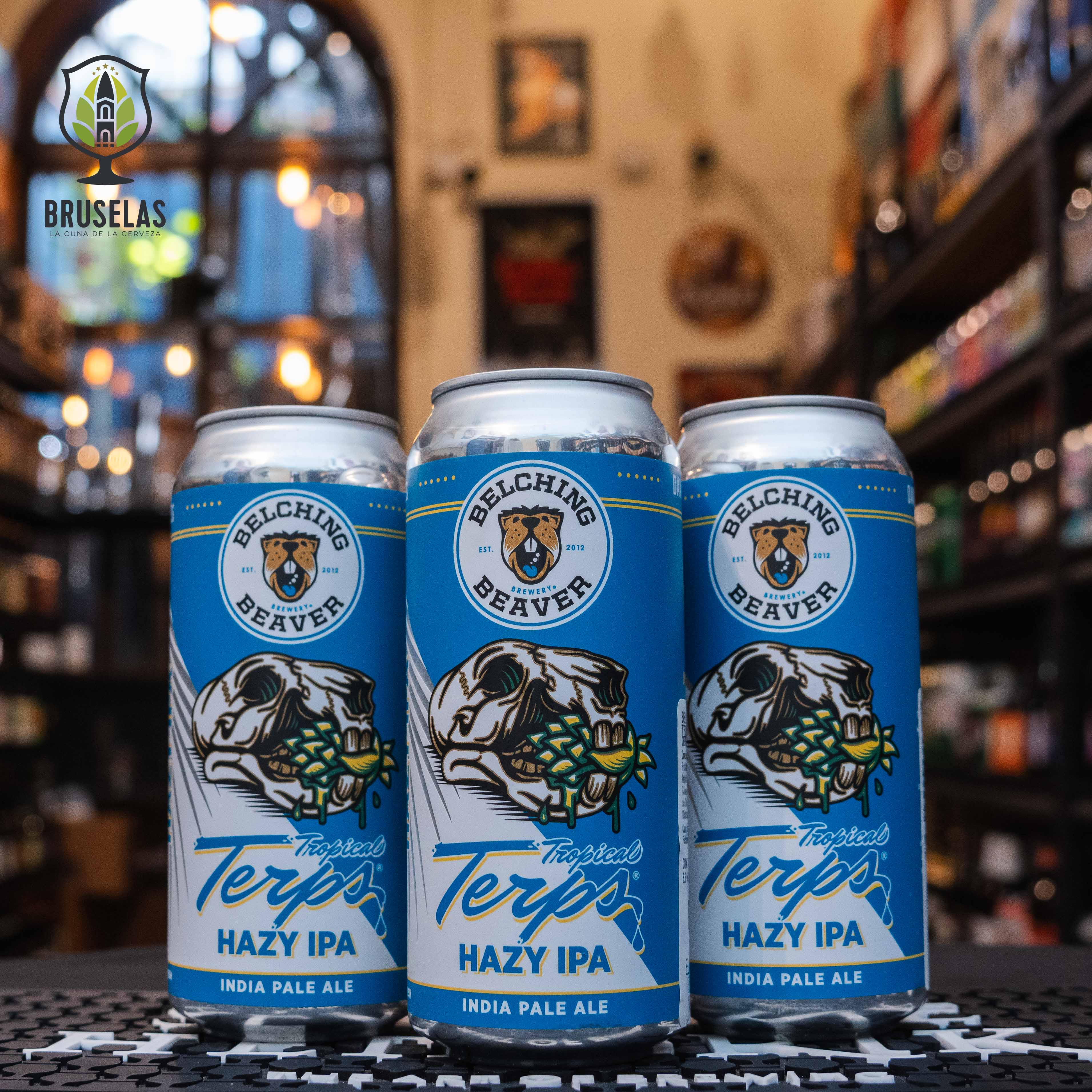  Belching Beaver Tropical Terps Hazy IPA, una cerveza estilo Hazy IPA de Belching Beaver Brewery. La lata tiene una etiqueta azul con un cráneo de castor sosteniendo lúpulos y el nombre en letras azules y blancas. Con un ABV de 6.6%, destaca por sus aromas a piña y mandarina. Ideal para acompañar mariscos y ensaladas frescas, reflejando un estilo frutal y refrescante.