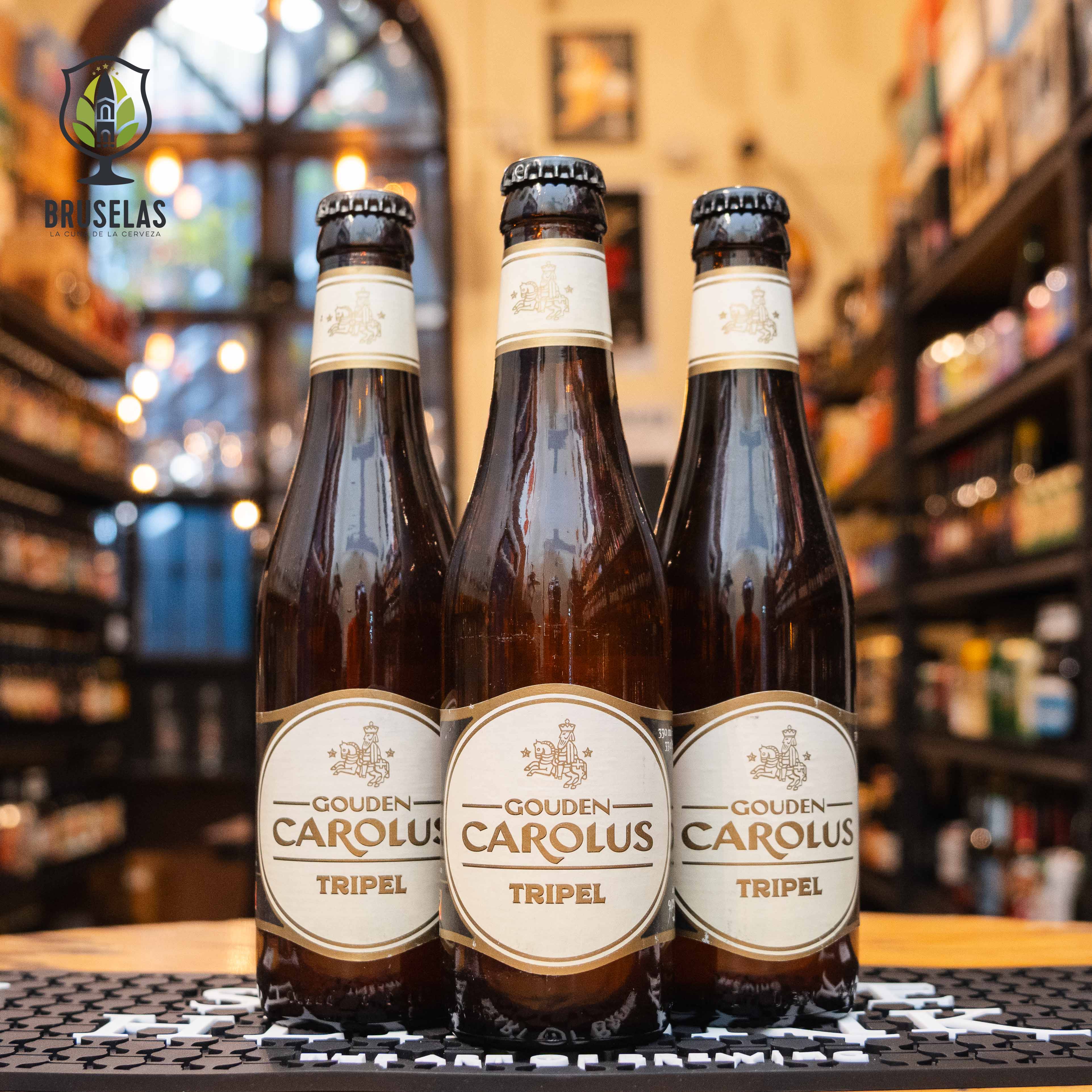 Botella de Gouden Carolus Tripel, una Belgian Tripel elaborada por Brouwerij Het Anker en Mechelen, Bélgica. La etiqueta es blanca y dorada, con el nombre en letras doradas. ABV de 9%, con un sabor equilibrado entre malta dulce, frutas como manzana y especias como clavo y pimienta blanca. Ideal para maridar con pescado, carnes blancas y quesos maduros. El diseño refleja la elegancia clásica de las cervezas belgas.