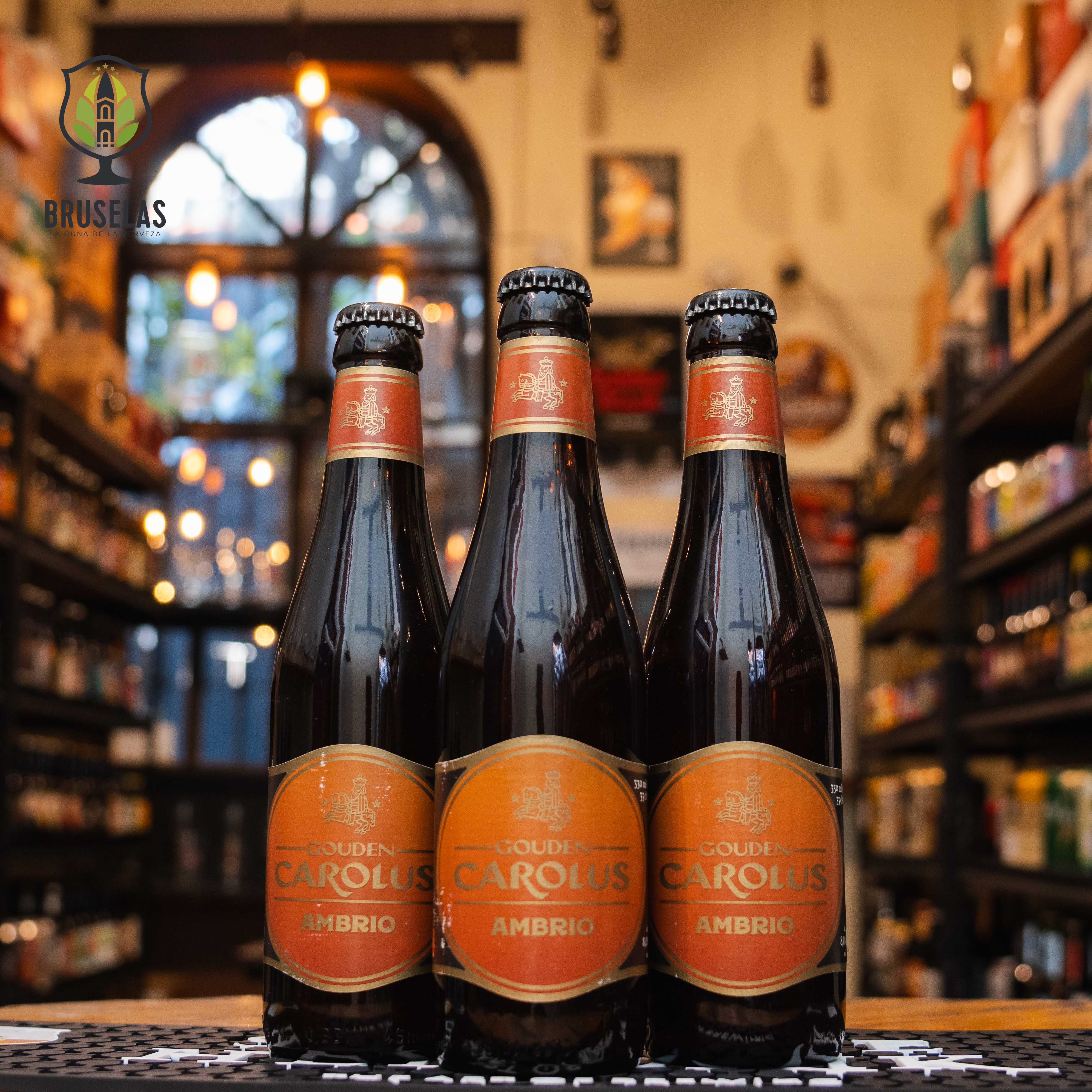 Botella de Gouden Carolus Ambrio, una Amber Ale belga elaborada por Brouwerij Het Anker. La etiqueta es dorada y roja, con el nombre en letras doradas. ABV de 8%, con un sabor equilibrado de caramelo, toffee y frutos secos. Ideal para acompañar carnes asadas, embutidos y quesos curados. El diseño de la botella refleja la tradición histórica de esta cerveza, con una receta que data de 1421.