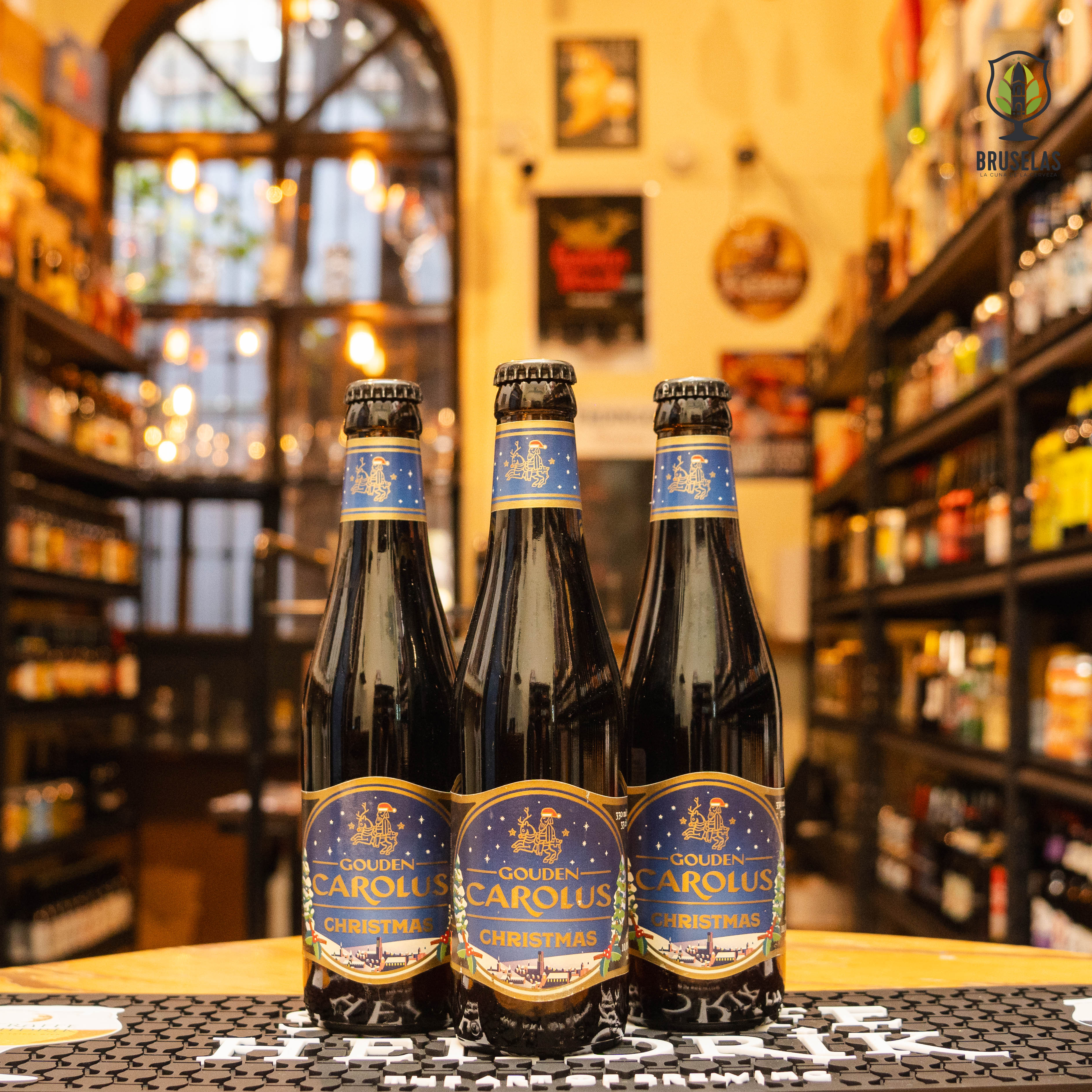 Botella de Gouden Carolus Christmas, una Belgian Strong Ale de Brouwerij Het Anker. La etiqueta tiene un diseño festivo en tonos oscuros y dorados. Con un ABV de 10.5%, ofrece aromas de frutas oscuras, caramelo y especias. Su sabor es equilibrado, con una base dulce de malta, amargor sutil y un final especiado. Ideal para acompañar estofados de carne, quesos fuertes y postres de chocolate. Su diseño refleja su carácter navideño.