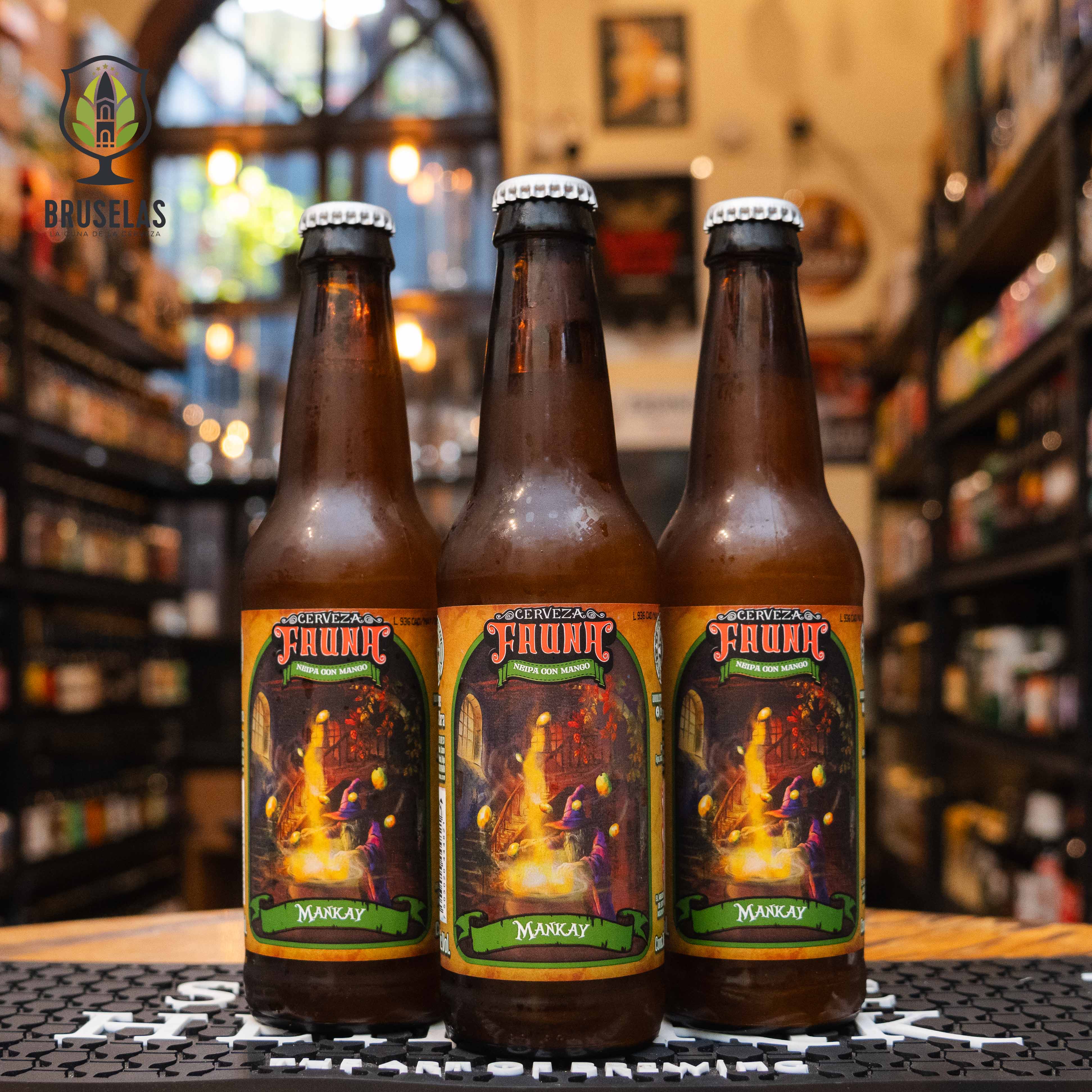 Botella de Fauna Mankay Hazy IPA, una cerveza artesanal mexicana de Cervecería Fauna con 7.0% ABV. La etiqueta tiene un diseño fantástico y colorido, evocando una atmósfera mística. Con aromas de mango, piña y cítricos, ofrece un sabor afrutado e intenso. Ideal para acompañar ceviches, tacos de pescado y platillos frescos. Su apariencia turbia y cuerpo sedoso la destacan como una auténtica Hazy IPA.