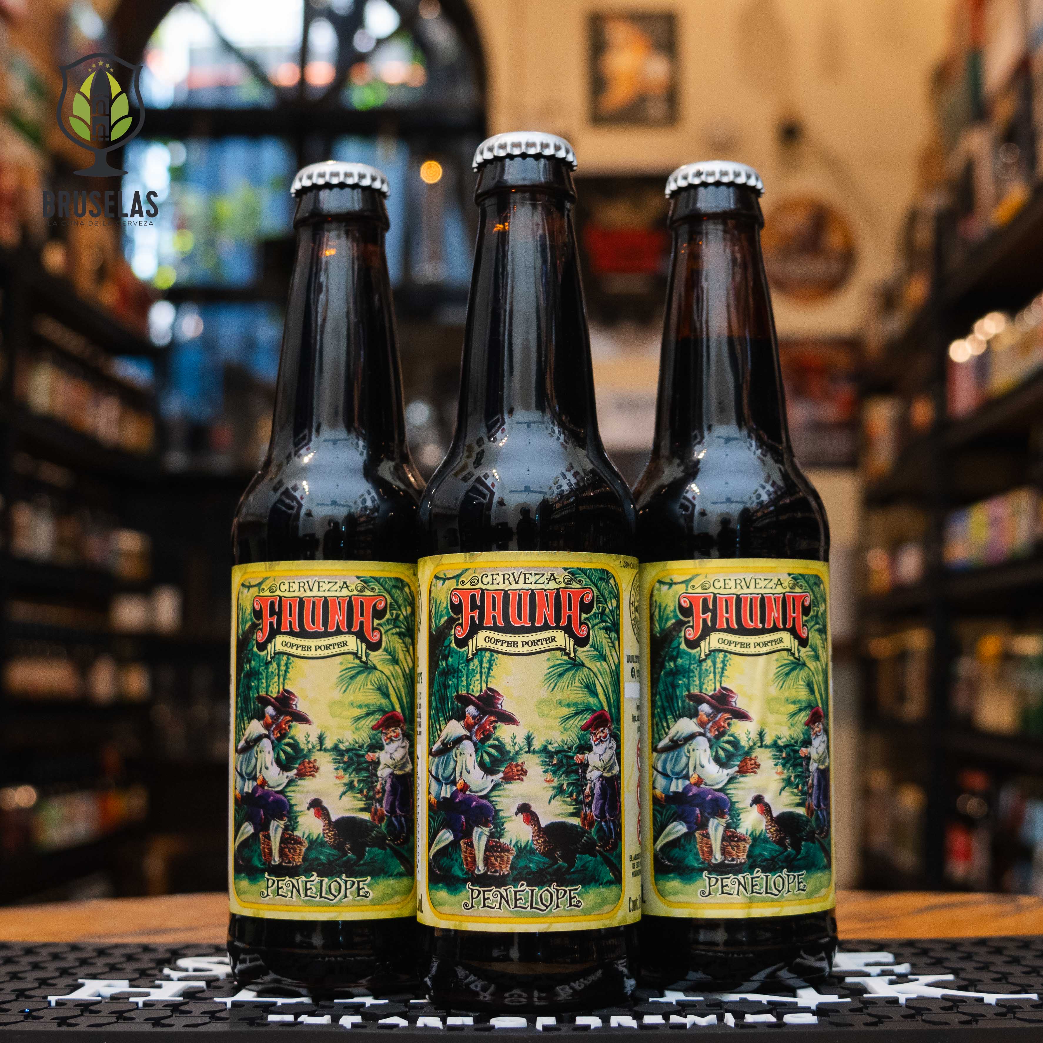 Botella de Fauna Penélope, una Coffee Porter de Cervecería Fauna, elaborada en Baja California. La etiqueta muestra una escena de personajes recolectando café en un entorno tropical. Con un ABV de 6.2%, ofrece aromas de café, chocolate y malta tostada, con sabores complejos y equilibrados. Ideal para acompañar postres de chocolate y nueces. El diseño refleja su carácter robusto y aromático.