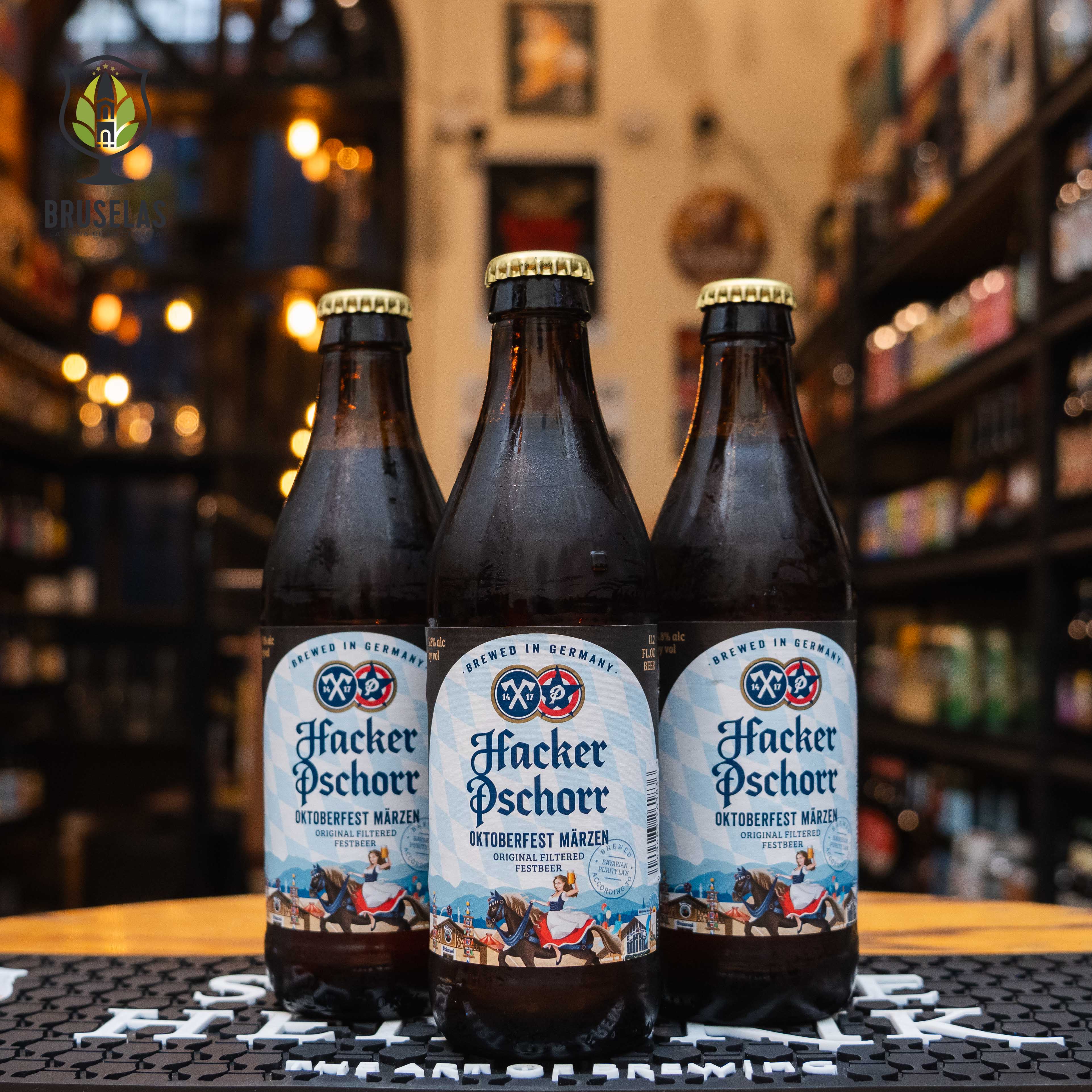 Botella de Hacker-Pschorr Oktoberfest Märzen, una cerveza de temporada elaborada en Múnich, Alemania, con un ABV de 5.8%. La etiqueta azul presenta una escena tradicional del Oktoberfest. Ofrece aromas a pan tostado y caramelo, con un sabor suave y maltoso. Ideal para maridar con pretzels, salchichas y chucrut. El diseño refleja la herencia bávara y la festividad del Oktoberfest.