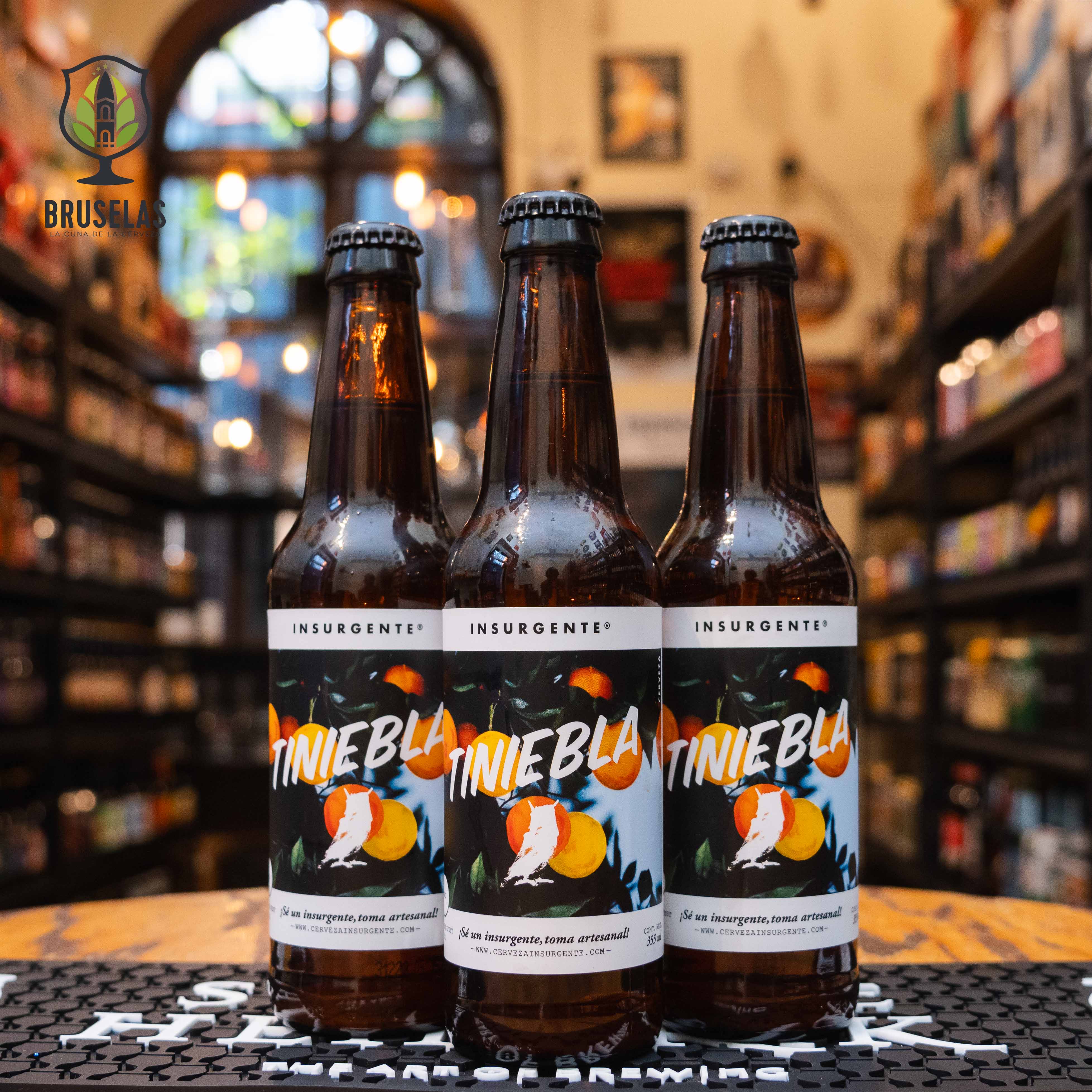 Botella de Insurgente Tiniebla, una Witbier de Cervecería Insurgente, elaborada en Baja California con un ABV de 5%. La etiqueta presenta un diseño colorido con una ilustración de cítricos y el nombre en letras blancas y naranjas. Esta cerveza es refrescante y ligera, con notas sutiles de lúpulo y una carbonatación viva. Ideal para acompañar mariscos, pescados y ceviches. Presentación de 355 ml.