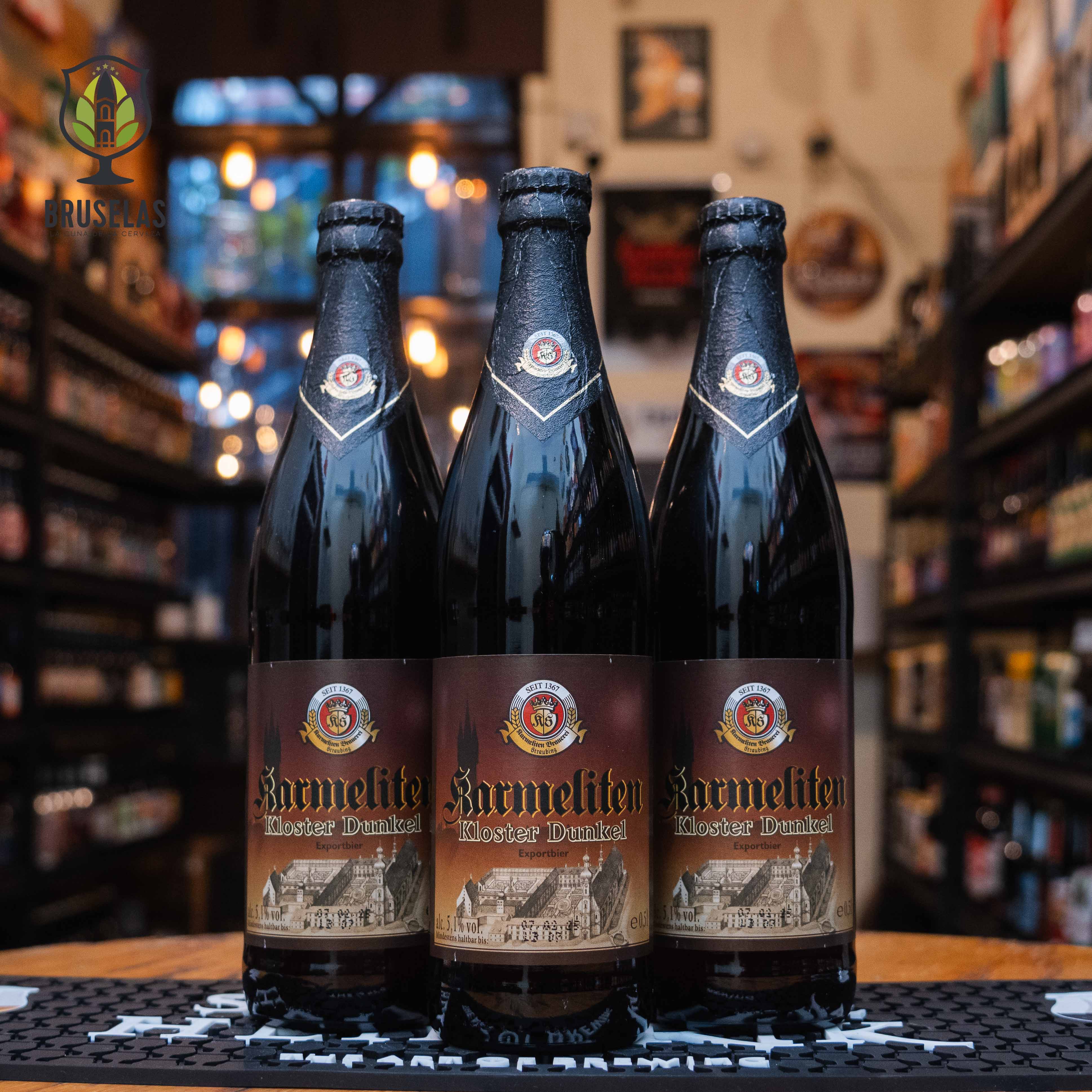 Botella de Karmeliten Kloster Dunkel, una cerveza estilo Dunkel elaborada por Karmeliten Brauerei en Alemania. Su etiqueta presenta tonos marrones y dorados con una ilustración del monasterio en la parte inferior, acompañada de detalles clásicos y el logo de la cervecería en la parte superior. Esta cerveza oscura de 5.0% ABV ofrece aromas a malta tostada, caramelo y frutas oscuras, con un sabor suave y equilibrado. Ideal para maridar con carnes asadas y quesos maduros. Presentación en botella de 500 ml.