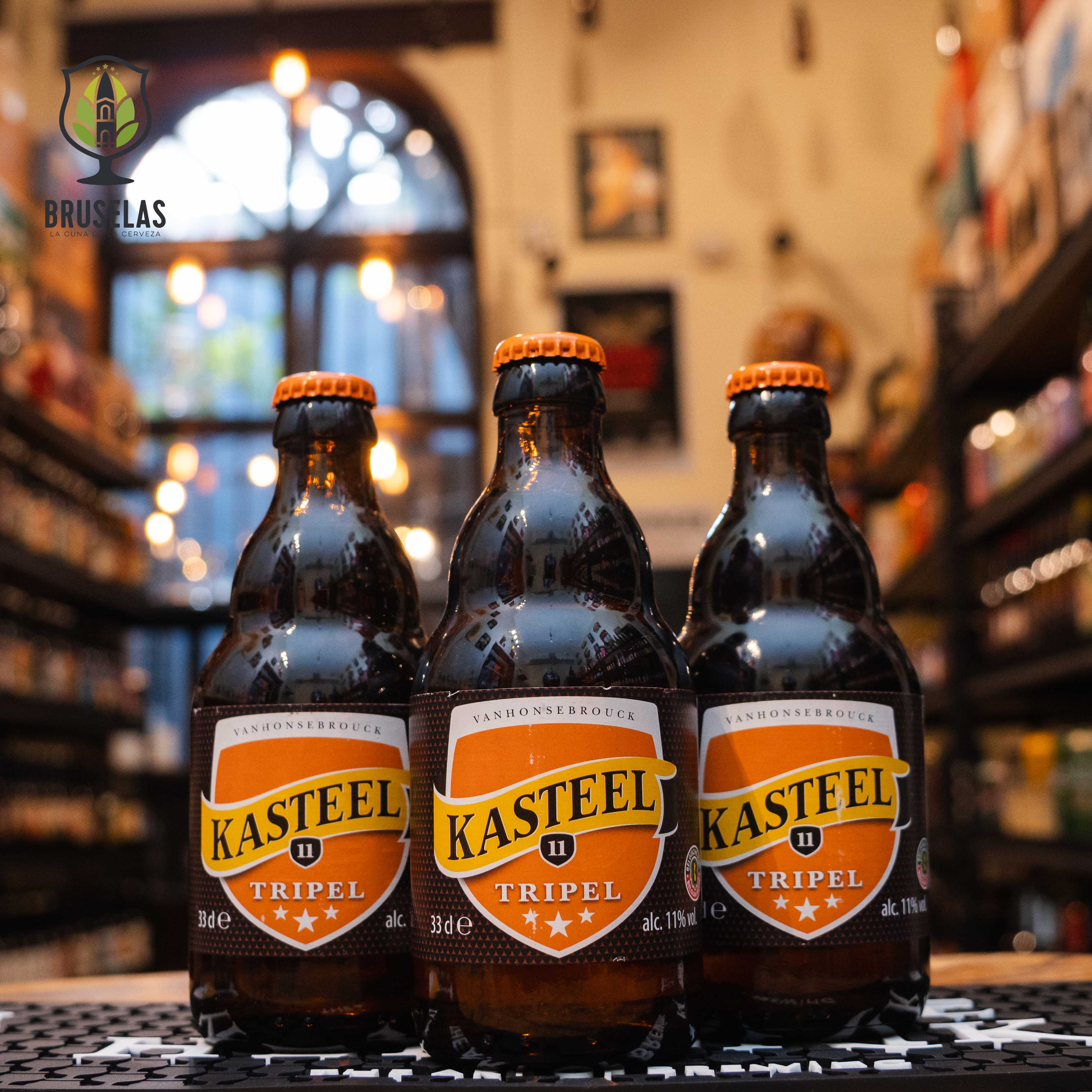 Botella de Kasteel Tripel, una Belgian Tripel de Kasteel Brouwerij Vanhonsebrouck. Con un ABV de 11%, tiene un color dorado intenso y espuma blanca cremosa. Ofrece aromas de frutas maduras, plátano y clavo. Su sabor combina dulzura maltosa con notas de manzana, pera y un toque especiado. Ideal para maridar con quesos fuertes, carnes blancas y platos especiados. El diseño refleja su carácter fuerte y equilibrado.