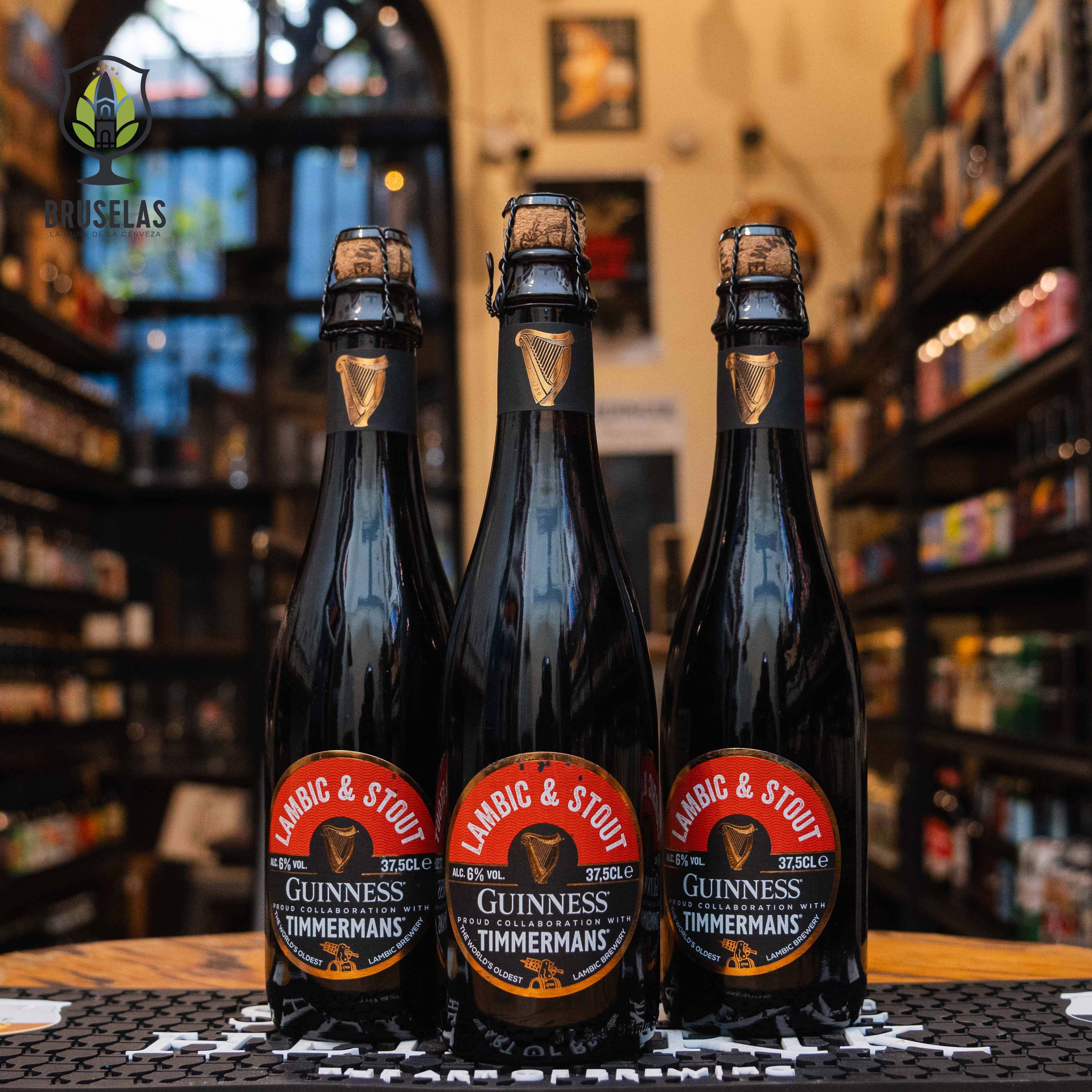 Botella de Guinness & Timmermans Lambic & Stout, una colaboración entre Guinness y Timmermans, elaborada en Bélgica. La etiqueta es negra y roja, con el logotipo dorado de Guinness al centro. El cierre de corcho está asegurado con alambre. Con un ABV de 6%, combina el carácter robusto del stout con la acidez del lambic. Ofrece sabores de chocolate y cerezas con un final seco. Ideal para acompañar carnes rojas y postres de chocolate.