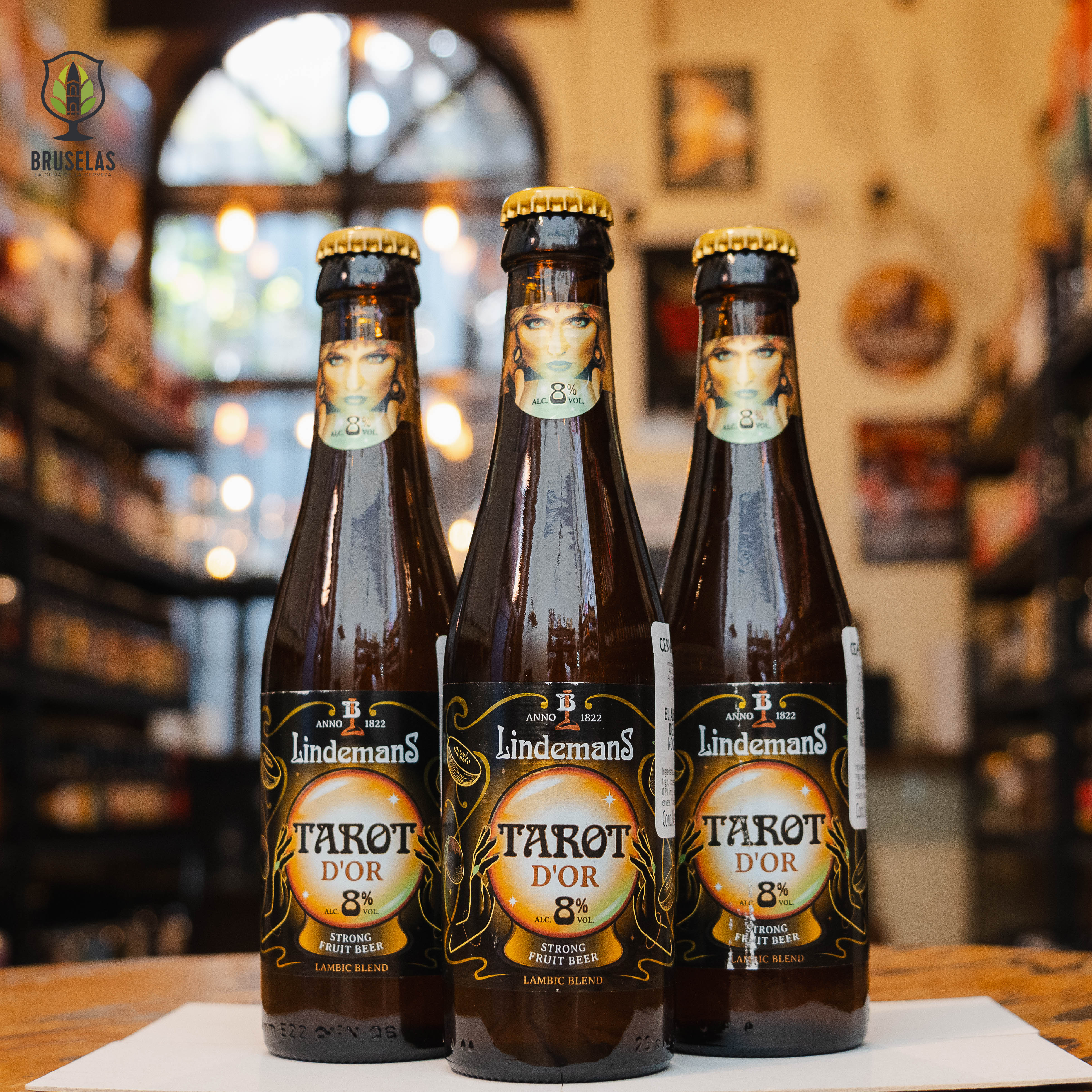 Botella de Lindemans Tarot d'Or, una Fruit Lambic belga de Brouwerij Lindemans. Con un ABV de 8%, presenta un color dorado y aromas intensos de frutas exóticas como mango, lychee y piña. Su sabor equilibra dulzura y acidez, con un final afrutado y fresco. Ideal para maridar con ensaladas de scampi y mango, pollo a la parrilla con piña y sorbetes de pera. Refleja frescura y carácter exótico.