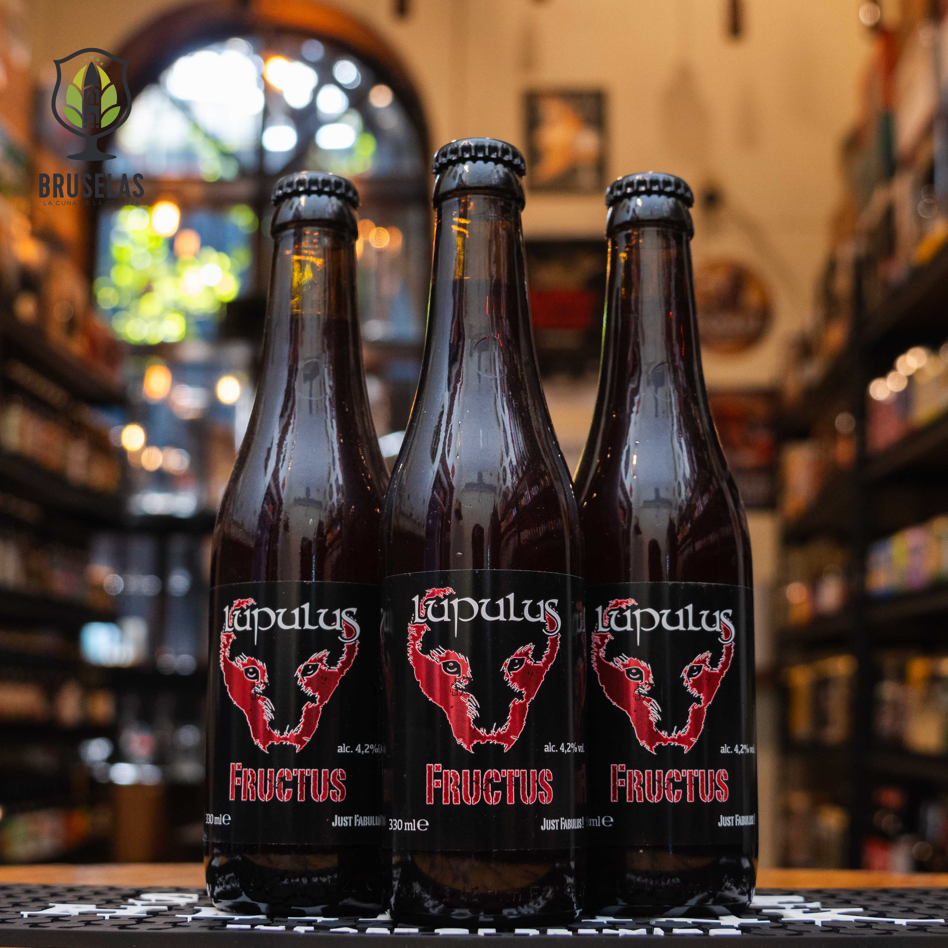 Botella de Lupulus Fructus, una cerveza estilo Fruit Beer de Brasserie Lupulus, elaborada en Bélgica. La etiqueta negra muestra un lobo estilizado en rojo, junto con el nombre 'Fructus' en letras rojas. Con un ABV de 4.2%, esta cerveza frutal presenta aromas a frambuesas y cerezas ácidas, con un sabor dulce y un toque especiado. Ideal para acompañar postres frutales, quesos suaves y ensaladas frescas.