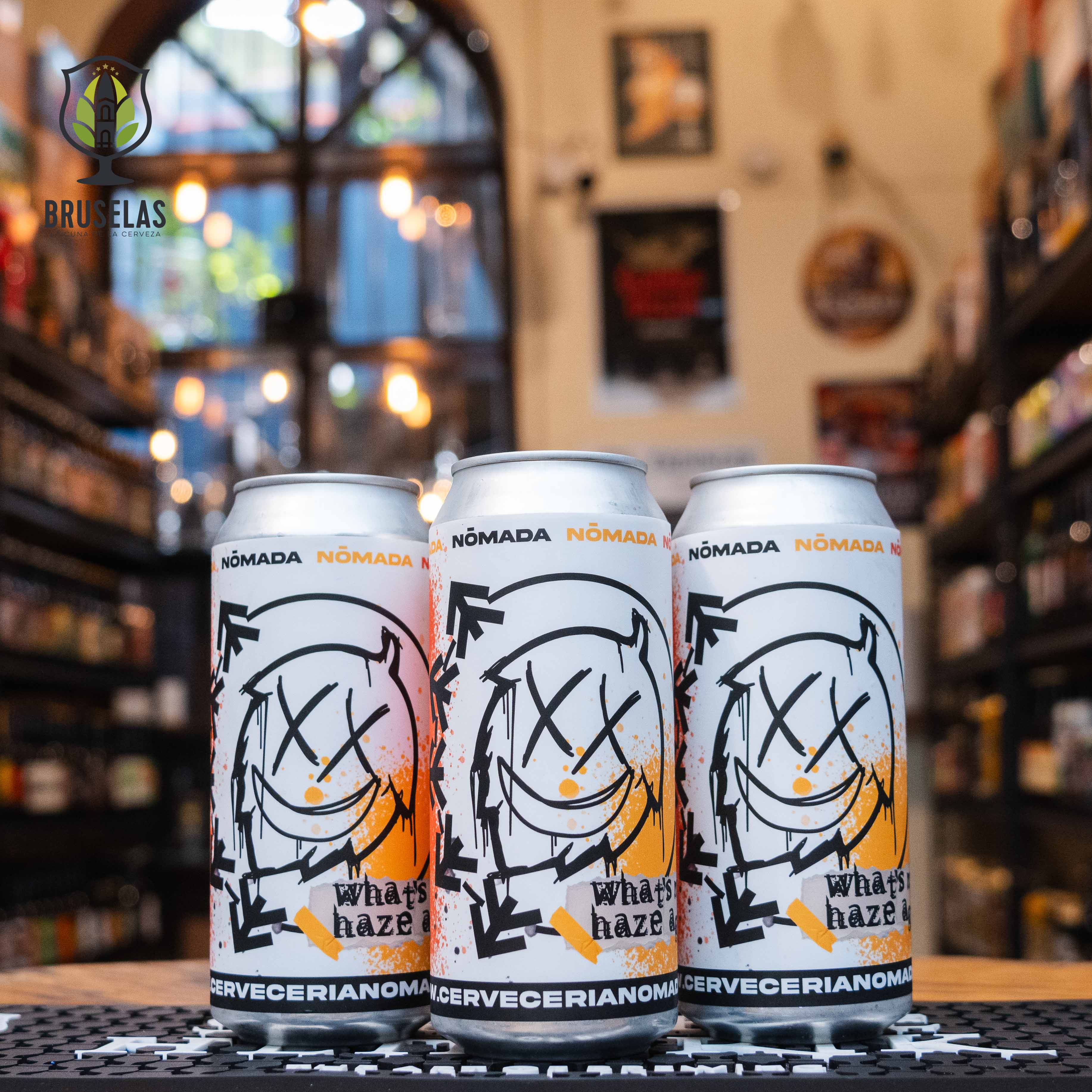 Lata de What's My Haze Again de Nómada Brewing, una Hazy IPA con un ABV aproximado de 8.2%. La etiqueta, inspirada en el logo de la banda Blink-182 y su canción 'What's My Age Again?', presenta un dibujo abstracto de una cara sonriente con ojos en forma de 'X'. Con notas tropicales de mango y piña, es ideal para acompañar mariscos. El diseño combina elementos musicales y modernos.