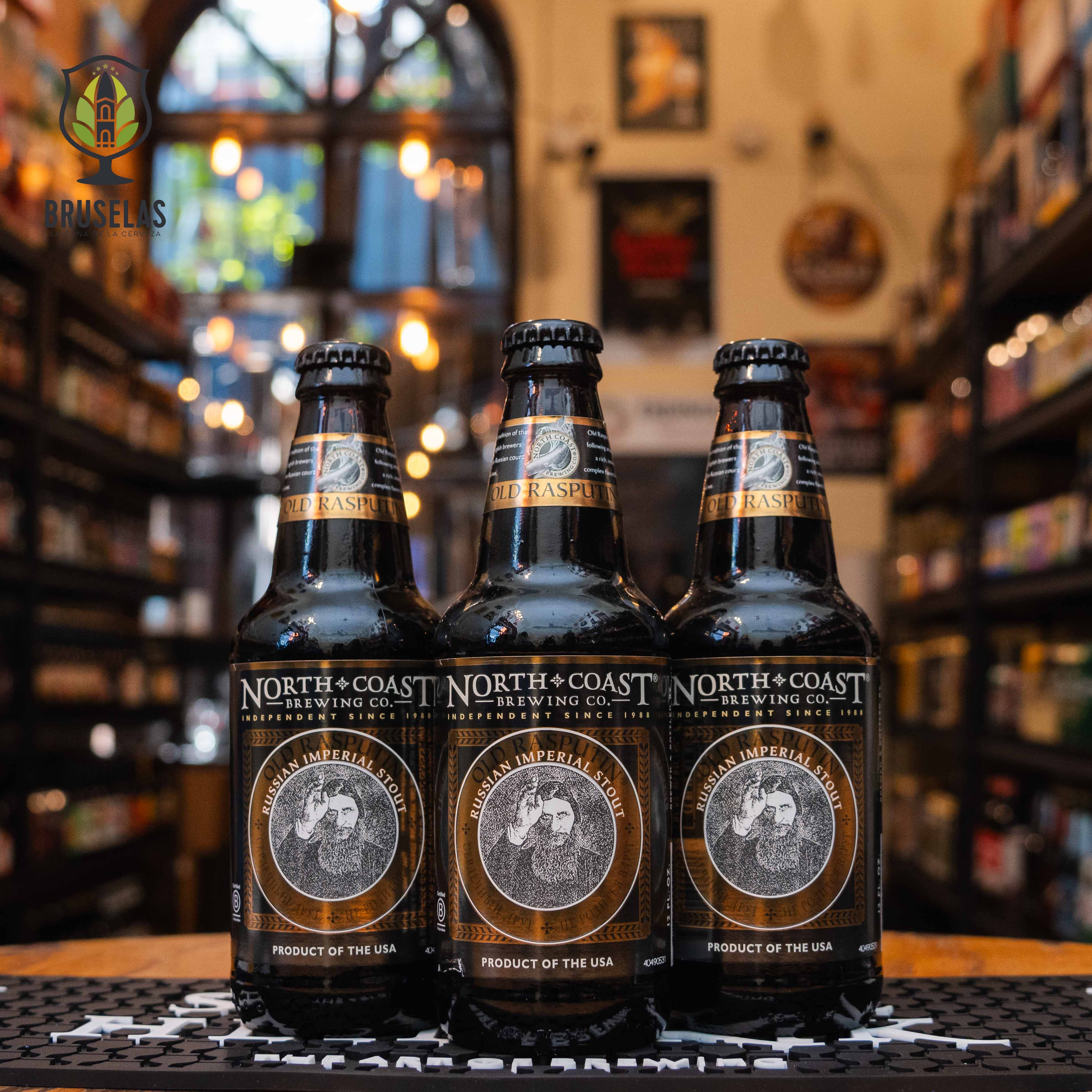 Botella de North Coast Old Rasputin, una Russian Imperial Stout de North Coast Brewing Company, con un ABV de 9.0%. Esta cerveza oscura ofrece un perfil de sabor intenso con notas a café tostado, chocolate oscuro y un toque sutil de regaliz. Su final es cálido y ligeramente amargo. Ideal para acompañar quesos fuertes, postres de chocolate y carnes ahumadas.