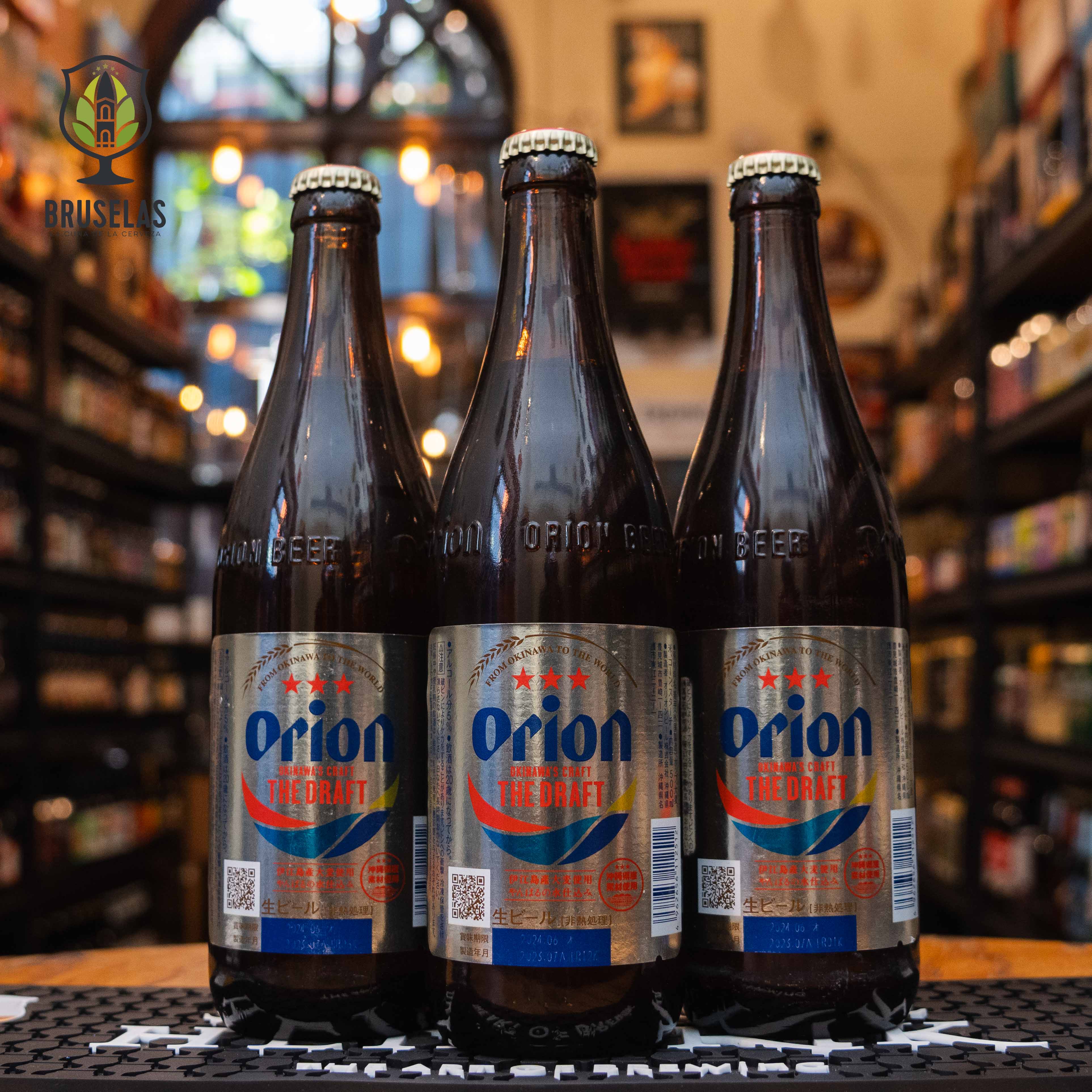 Botella de Orion The Draft, una Japanese Rice Lager de Orion Breweries, Ltd., elaborada en Okinawa, Japón. La etiqueta plateada presenta detalles en rojo y azul con el logotipo de Orion en letras azules. Esta lager tiene un ABV de 5.0% y ofrece un sabor suave con toques de arroz y un final seco y refrescante. Ideal para maridar con sushi, tempura y platos ligeros de la cocina asiática.