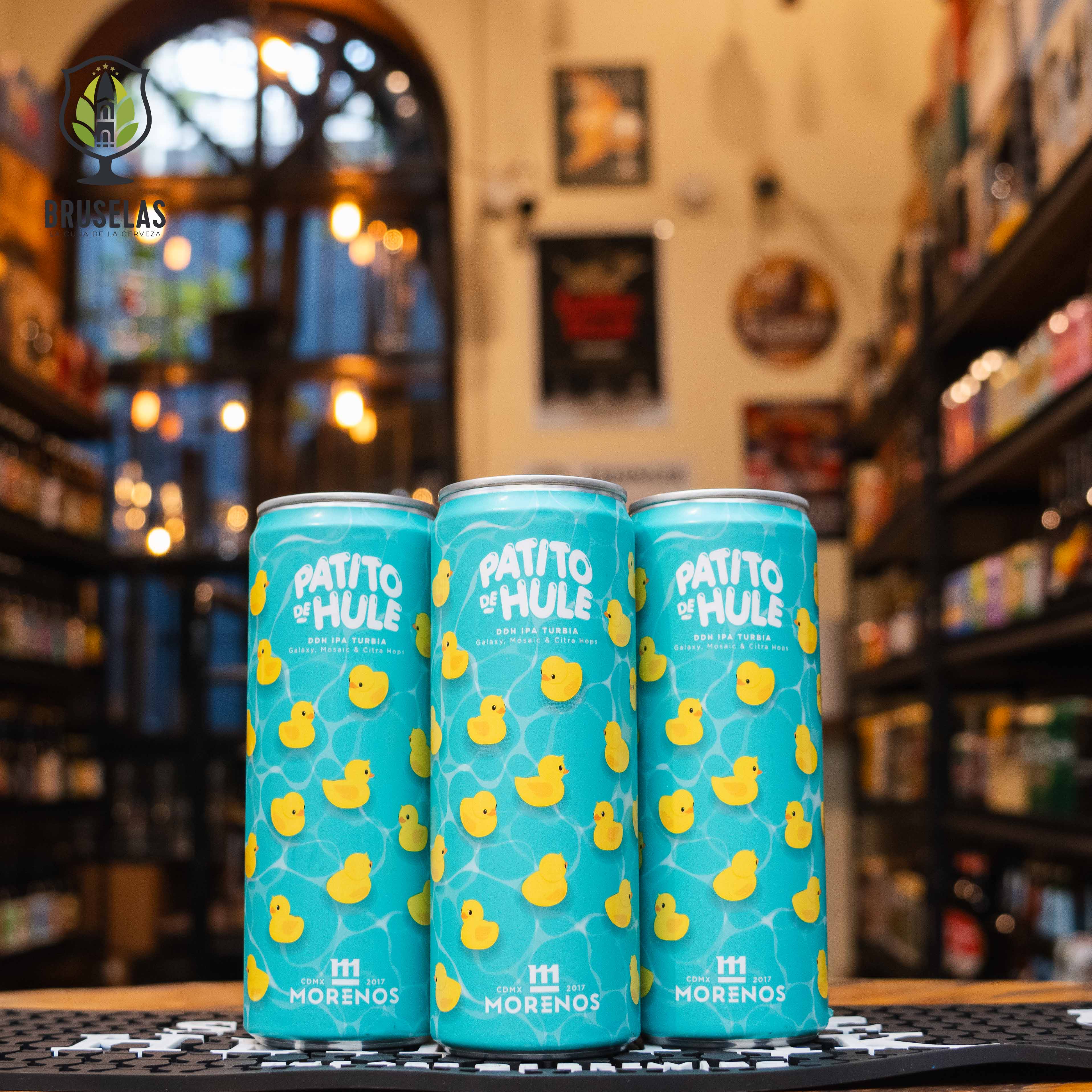 Cerveza Patito de Hule, una New England IPA (NEIPA) de Cervecería Morenos. Su etiqueta azul presenta un patrón de patitos de hule amarillos, resaltando su estilo divertido y vibrante. Con un ABV de 6.2% y 50 IBU, esta IPA turbia ofrece intensos aromas frutales de arándanos, papaya y mandarina. Su sabor es jugoso y suave, equilibrando bien el amargor. Ideal para maridar con hamburguesas gourmet y tacos de pescado.