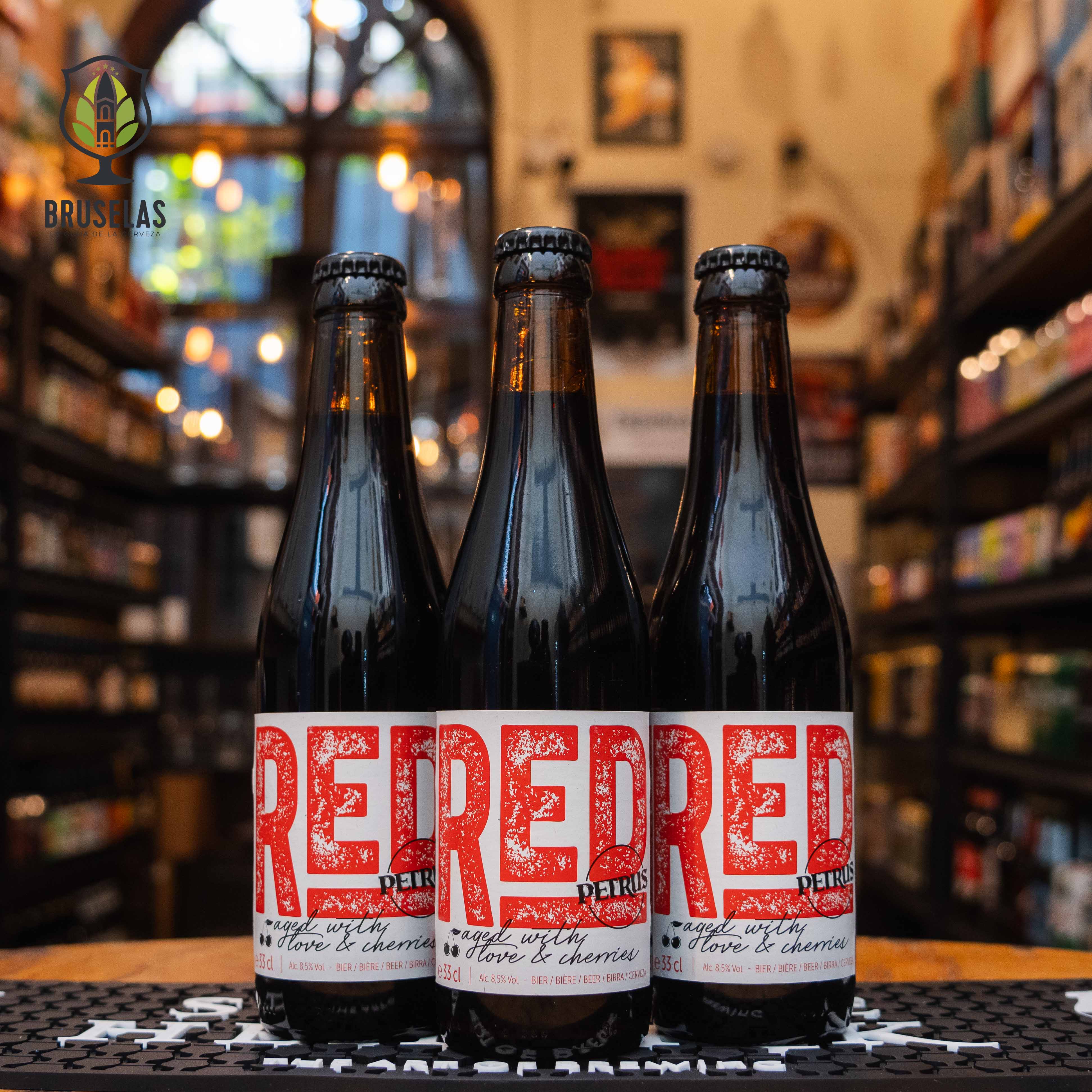 Botella de Petrus Red, una cerveza belga estilo Sour Ale con frutas elaborada por Brouwerij De Brabandere, Bélgica. La etiqueta es blanca con la palabra "RED" en grande, en un estilo gráfico de color rojo que resalta sobre el fondo claro. Presenta un ABV de 8.5%, con sabores agridulces dominados por cerezas y un toque de madera debido a su maduración en barricas de roble. Ideal para acompañar tartar de pescado, carnes curadas y postres frutales.