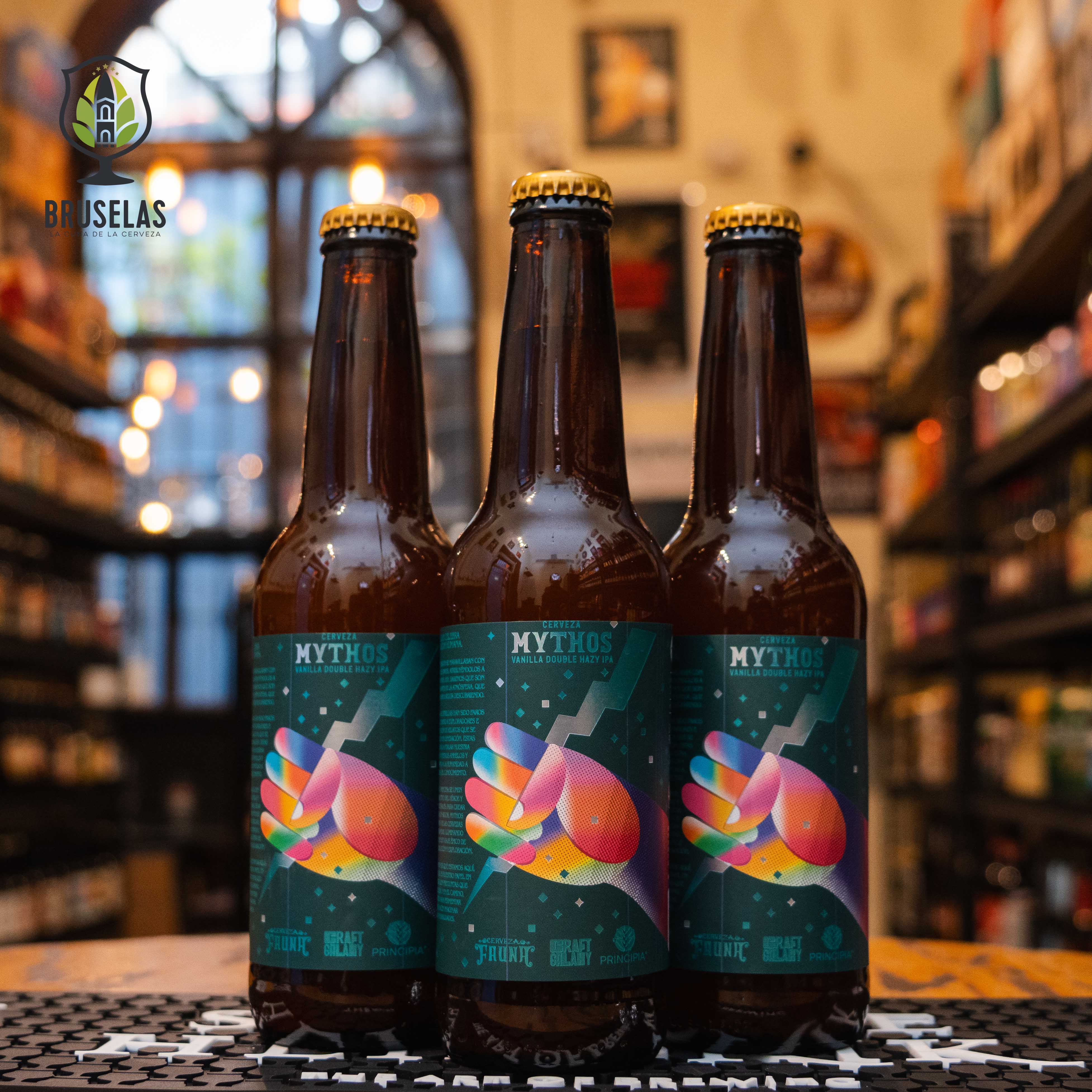 Botella de Principia Mythos, una Vanilla Double Hazy IPA de Cervecería Principia con un ABV de 8.2%. Ofrece aromas intensos de mango, piña y un toque de vainilla. Su sabor combina la dulzura de la vainilla con el amargor y las notas cítricas de los lúpulos, en un cuerpo cremoso. Ideal para maridar con postres como tarta de limón, pasteles con crema o platos picantes. Refleja innovación y complejidad.