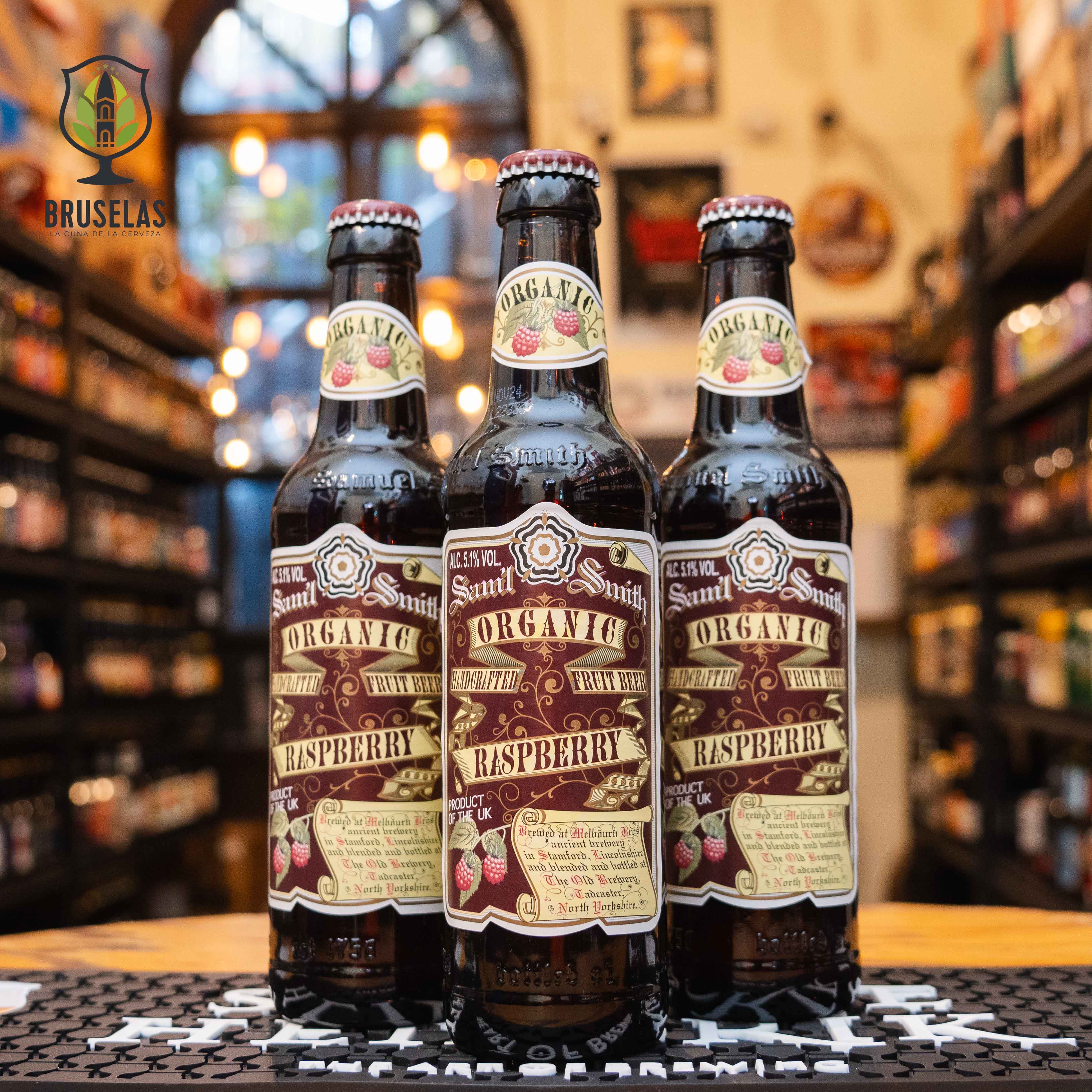 Botella de Samuel Smith Organic Raspberry, una Fruit Beer inglesa de Samuel Smith Old Brewery. La etiqueta es marrón con detalles frutales de frambuesa y letras clásicas. ABV de 5.1%, con aromas de frambuesa fresca y malta suave. Sabor dulce y afrutado con una acidez balanceada. Ideal para acompañar postres frutales, ensaladas con queso de cabra y tartas de frutas. Diseño orgánico y artesanal.