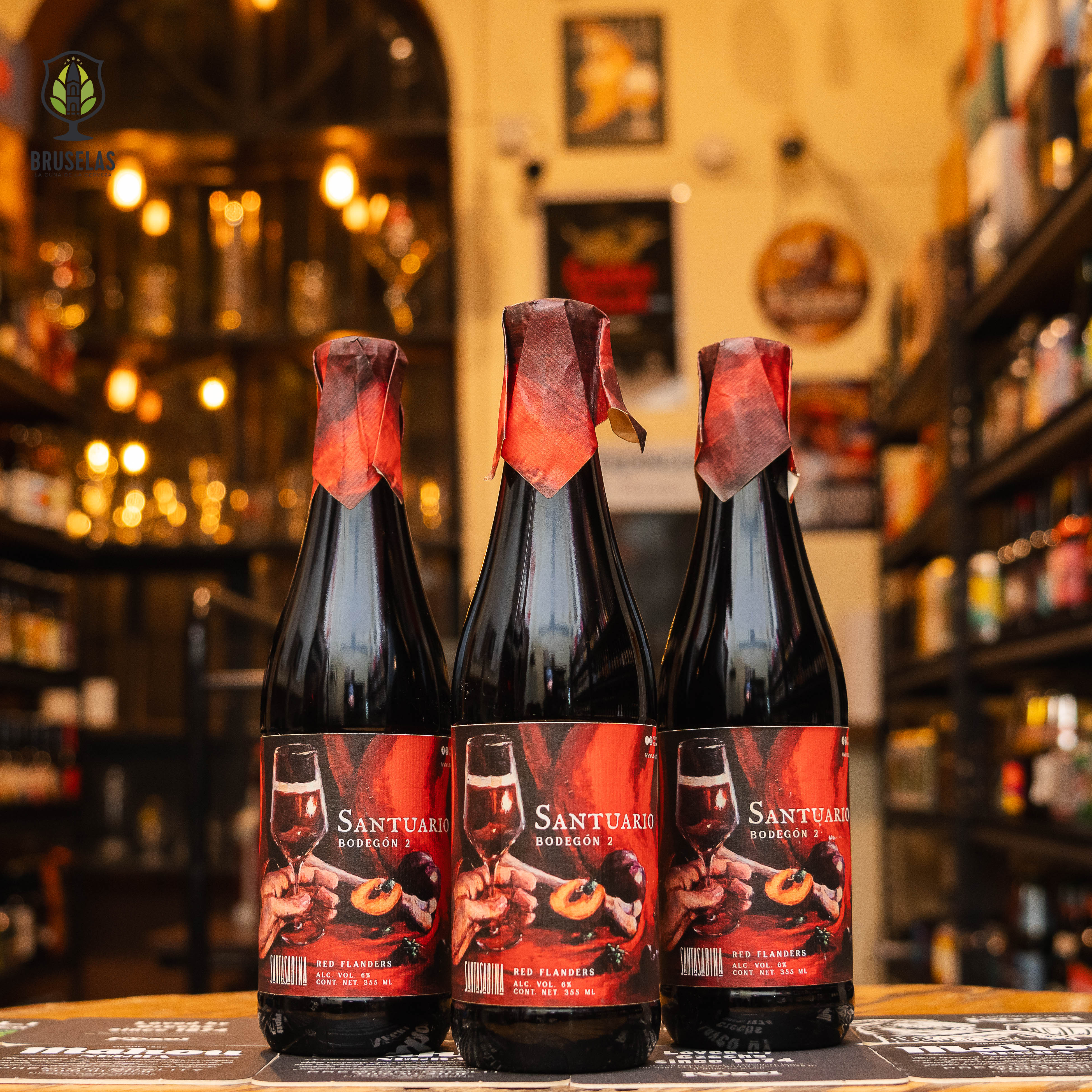 Botella de Santa Sabina Santuario Bodegón 2, una Flanders Red Ale con un ABV de 6.0%. Esta cerveza destaca por su perfil ácido y afrutado, con notas de ciruela y cereza ácida. Madurada en barricas de roble, presenta una complejidad que recuerda a un buen vino tinto. Ideal para maridar con quesos añejos, carnes curadas y platos con frutas secas, perfecta para los amantes de cervezas ácidas y añejadas.