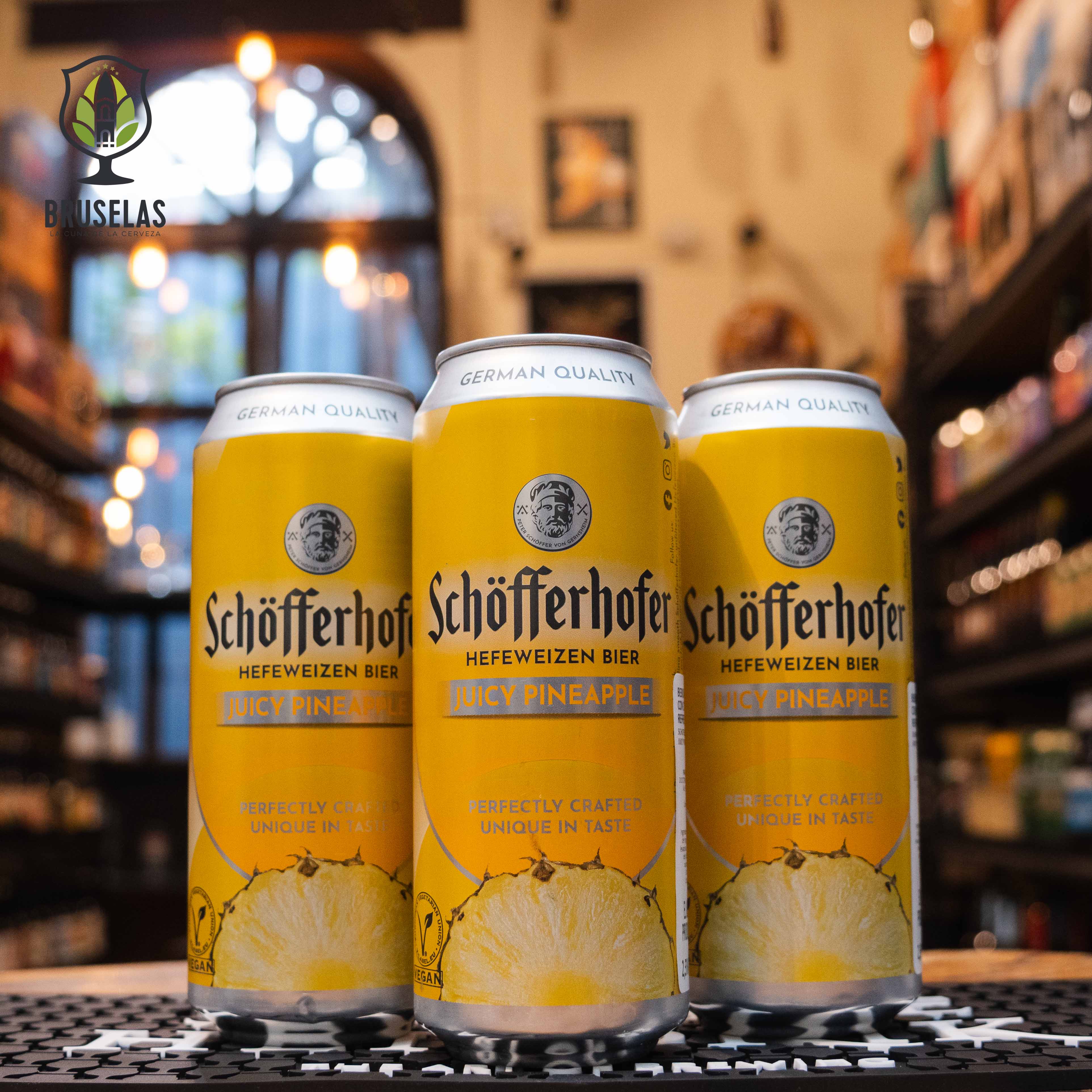 Botella de Schöfferhofer Piña, una Radler que mezcla cerveza de trigo Hefeweizen con jugo de piña. Con un ABV de 2.5%, destaca por su aroma a piña intensa y sutil fondo de trigo. Su sabor dulce y refrescante equilibra la acidez de la piña con el cuerpo suave de la cerveza. Ideal como aperitivo o acompañada de ensaladas frescas, quesos suaves y platos ligeros. Perfecta para disfrutar en climas cálidos.