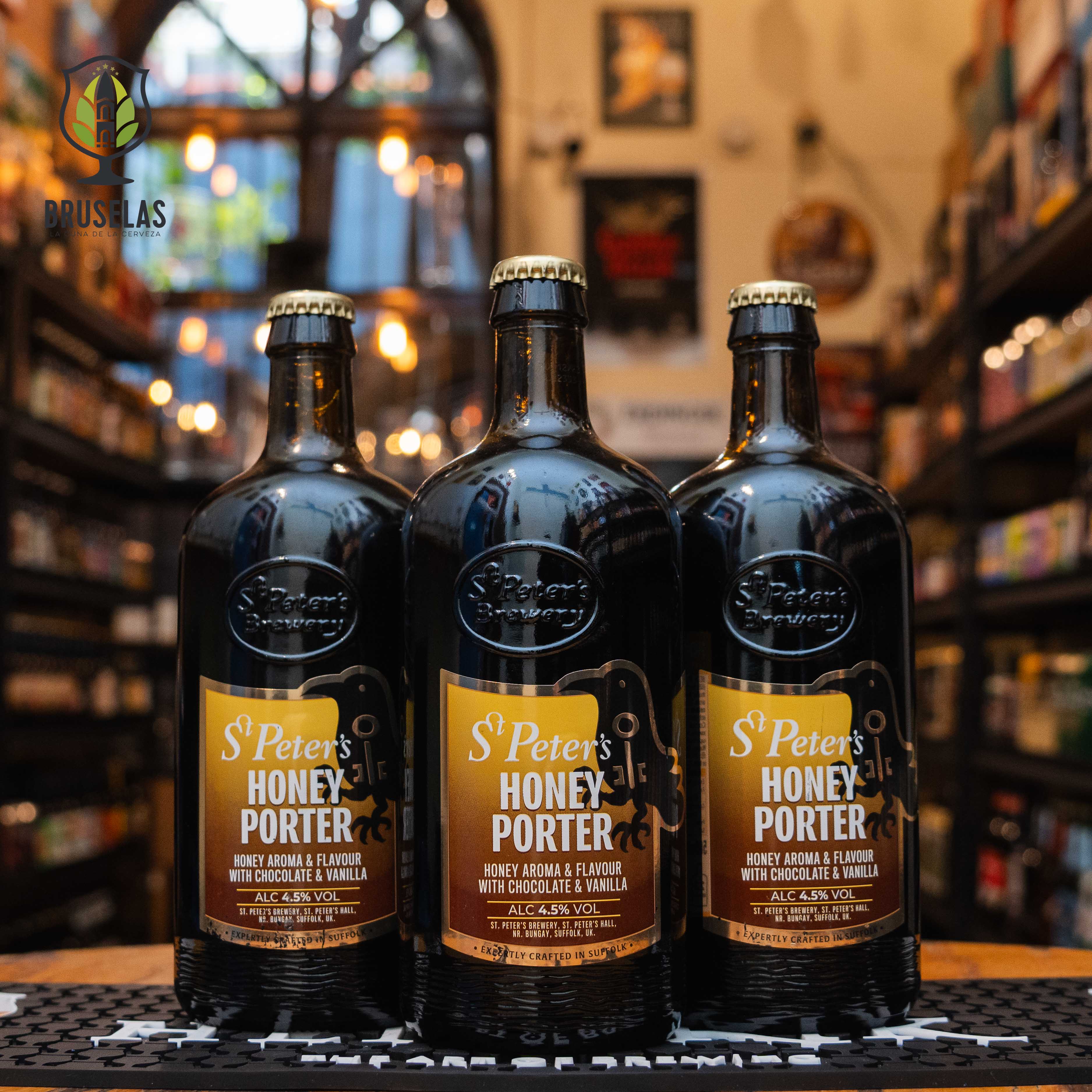 Botella de St. Peter's Honey Porter, una cerveza estilo English Porter de St. Peter's Brewery en Suffolk, Inglaterra, con un ABV de 4.5%. La etiqueta es dorada y negra con detalles en blanco. Su color es rojo ámbar profundo, y ofrece aromas a miel, chocolate y vainilla. En boca, se aprecian sabores de maltas tostadas y chocolate equilibrados con la dulzura de la miel. Ideal para maridar con postres de chocolate y quesos maduros.