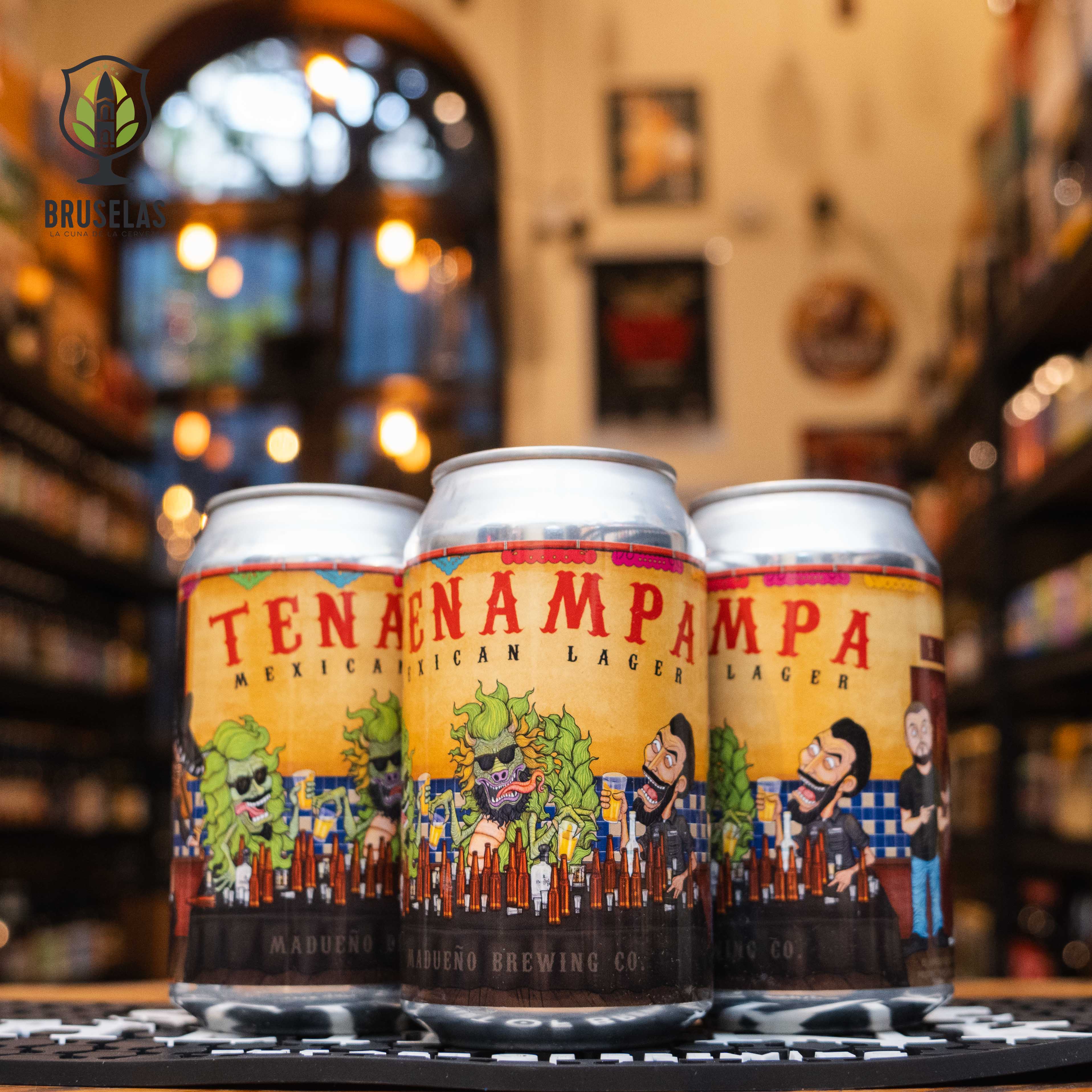 Lata de Madueño Tenampa Mexican Lager, elaborada por Madueño Brewing Co. La etiqueta es colorida, con ilustraciones de personajes festivos y elementos mexicanos. El nombre está en letras rojas grandes. ABV aproximado de 5%. Sabor refrescante con notas de agave y hierbas. Ideal para acompañar tacos y quesadillas. Diseño divertido que refleja la cultura mexicana.