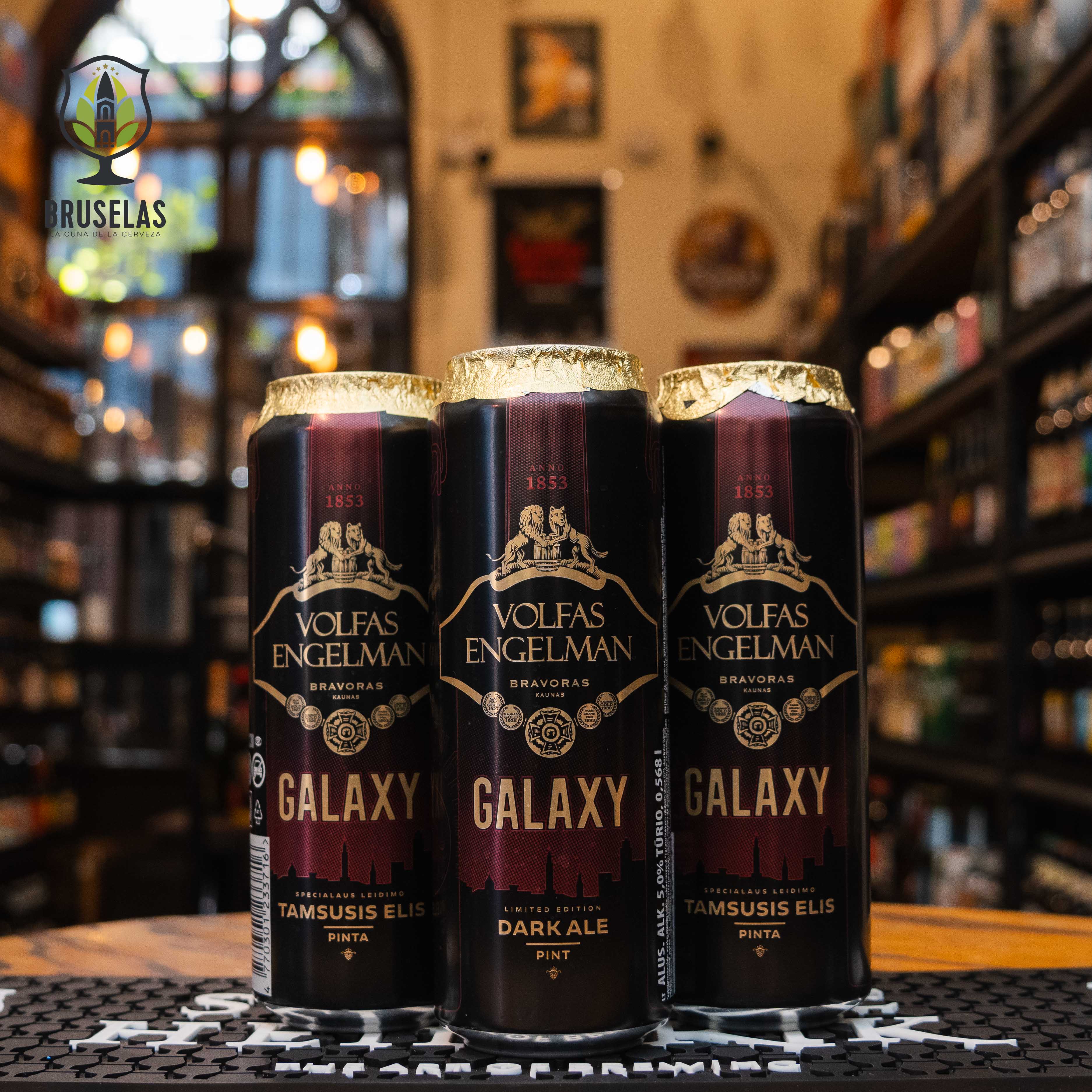 Lata de Volfas Engelman Galaxy Dark Ale, una ale oscura lituana. La etiqueta es negra con detalles dorados y rojos, destacando el nombre en letras grandes. ABV de 5%. Sabor equilibrado con notas de malta caramelizada y un ligero amargor del lúpulo Galaxy. Ideal para acompañar carnes a la parrilla y quesos maduros. El diseño refleja la calidad tradicional y el enfoque innovador de la cervecería.