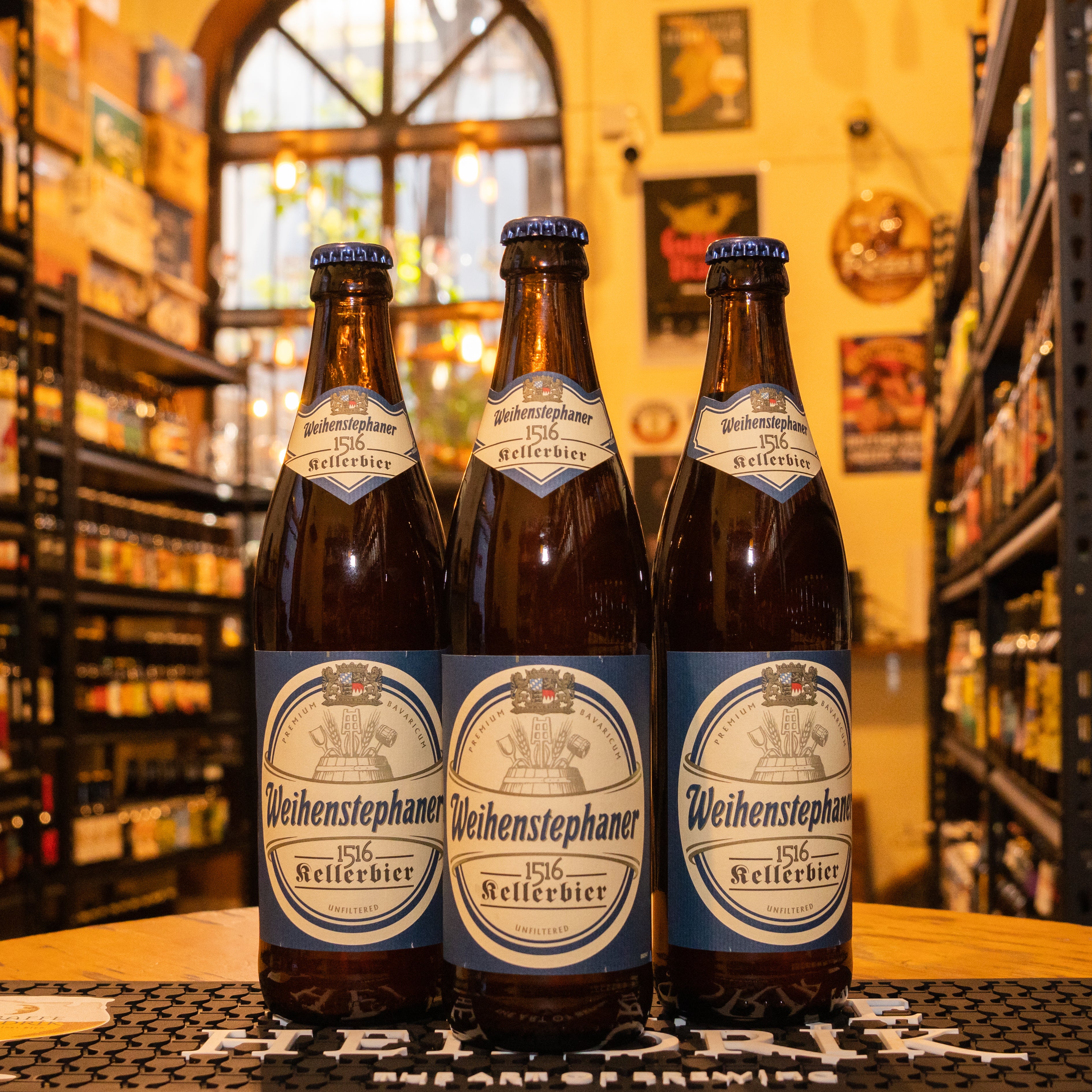 Botella de Weihenstephaner 1516 Kellerbier, una cerveza sin filtrar estilo Kellerbier con un ABV de 5.6%, elaborada por la cervecería más antigua del mundo, Weihenstephan. Presenta aromas a malta con notas de caramelo y lúpulo fresco, mientras que su sabor es suave y equilibrado, con un ligero toque de dulzor. Ideal para maridar con salchichas, pretzels y quesos, reflejando la auténtica tradición cervecera bávara.