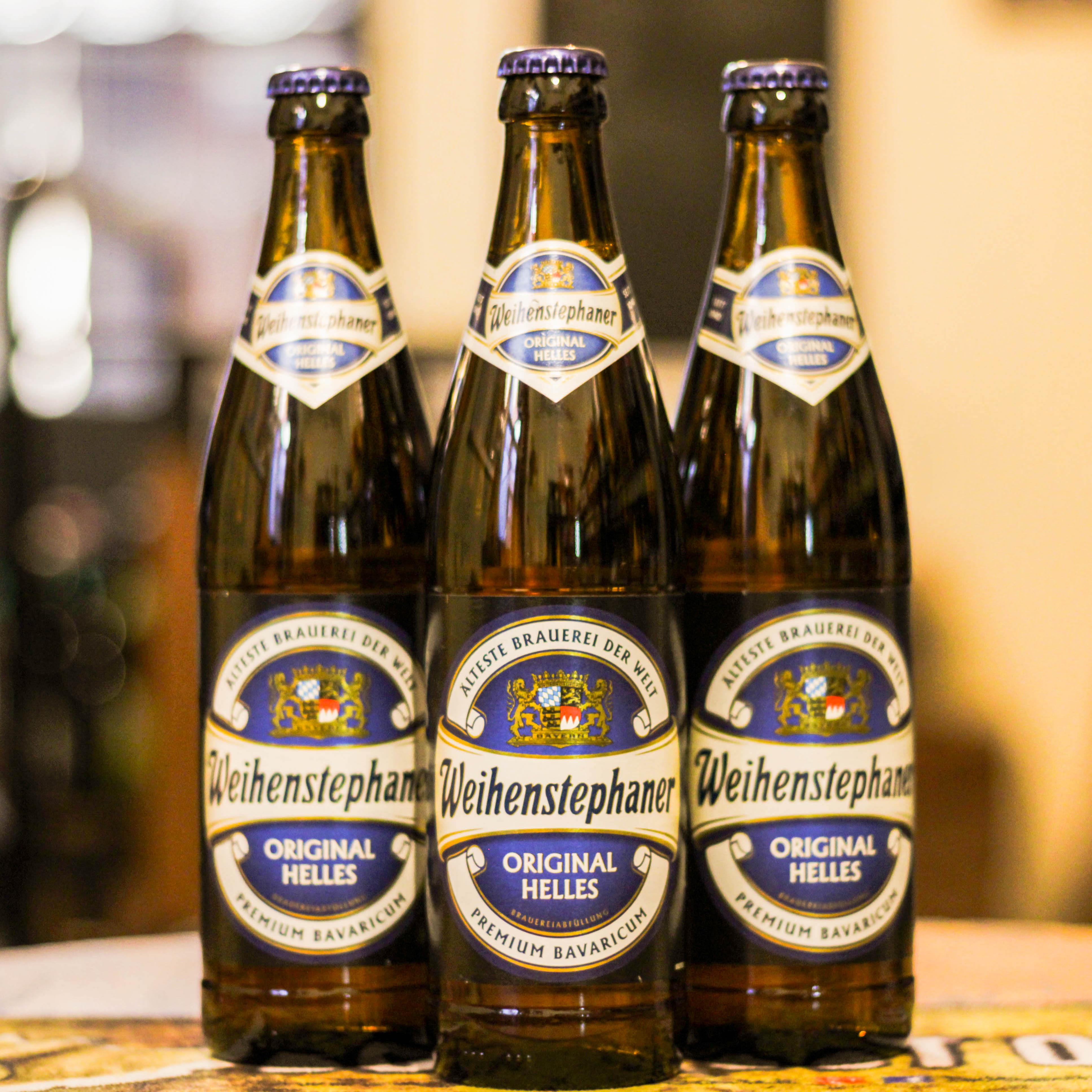 Botella de Weihenstephaner Original Helles, una lager Helles elaborada por la cervecería Weihenstephan en Alemania. La etiqueta muestra el escudo en dorado, con detalles en azul y blanco. ABV de 5.1%, sabor maltoso suave con lúpulo ligero y final limpio. Ideal con ensaladas, aves y guisos. Refleja la herencia de la cervecería más antigua del mundo.