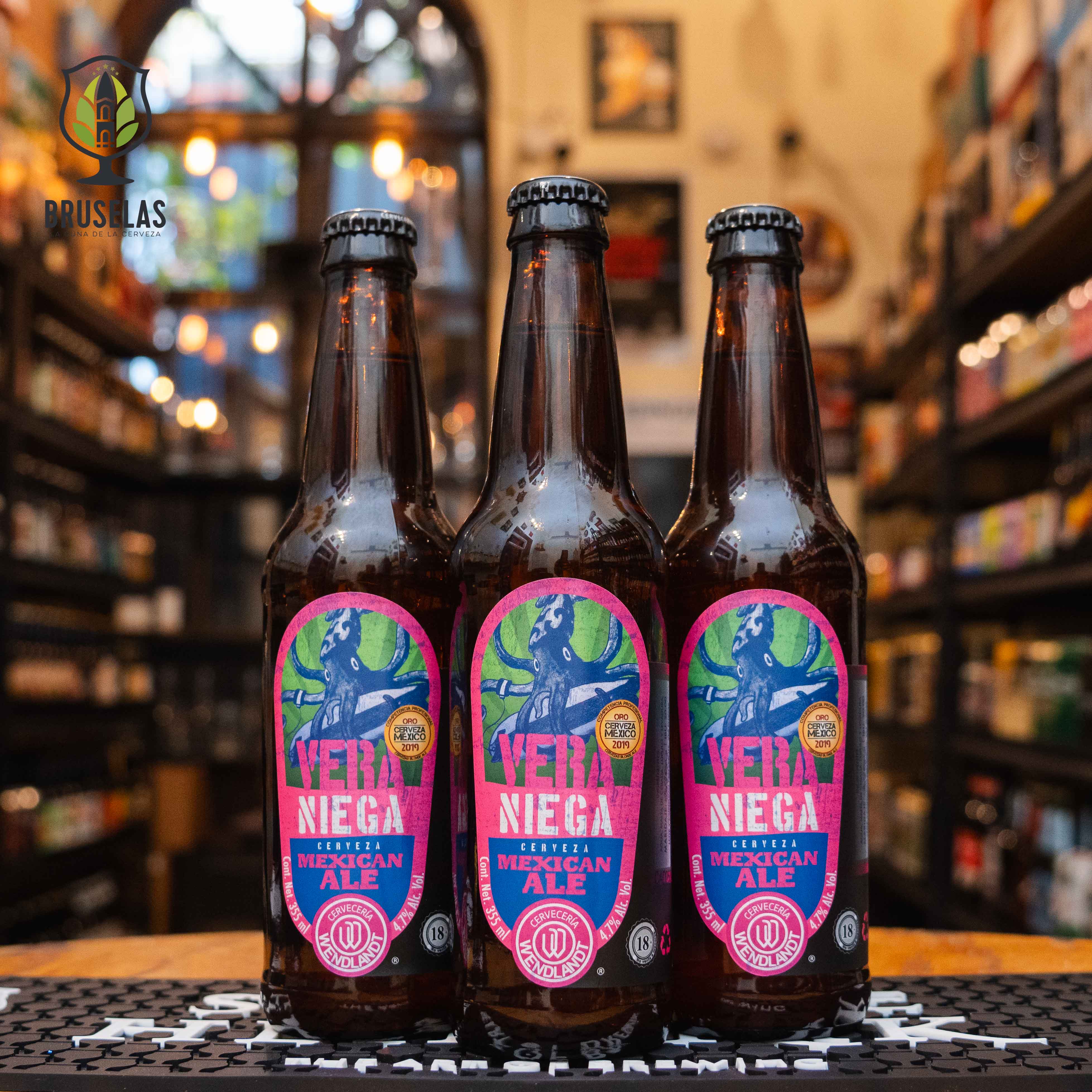 Botella de Wendlandt Veraniega, una Mexican Ale artesanal de Cervecería Wendlandt. La etiqueta es rosa y azul con una ilustración de estilo vintage. ABV de 4.5%. Sabor suave y refrescante con notas florales y cítricas. Ideal para acompañar mariscos, aves y ensaladas frescas. El diseño refleja un estilo veraniego y ligero, perfecto para cualquier ocasión.