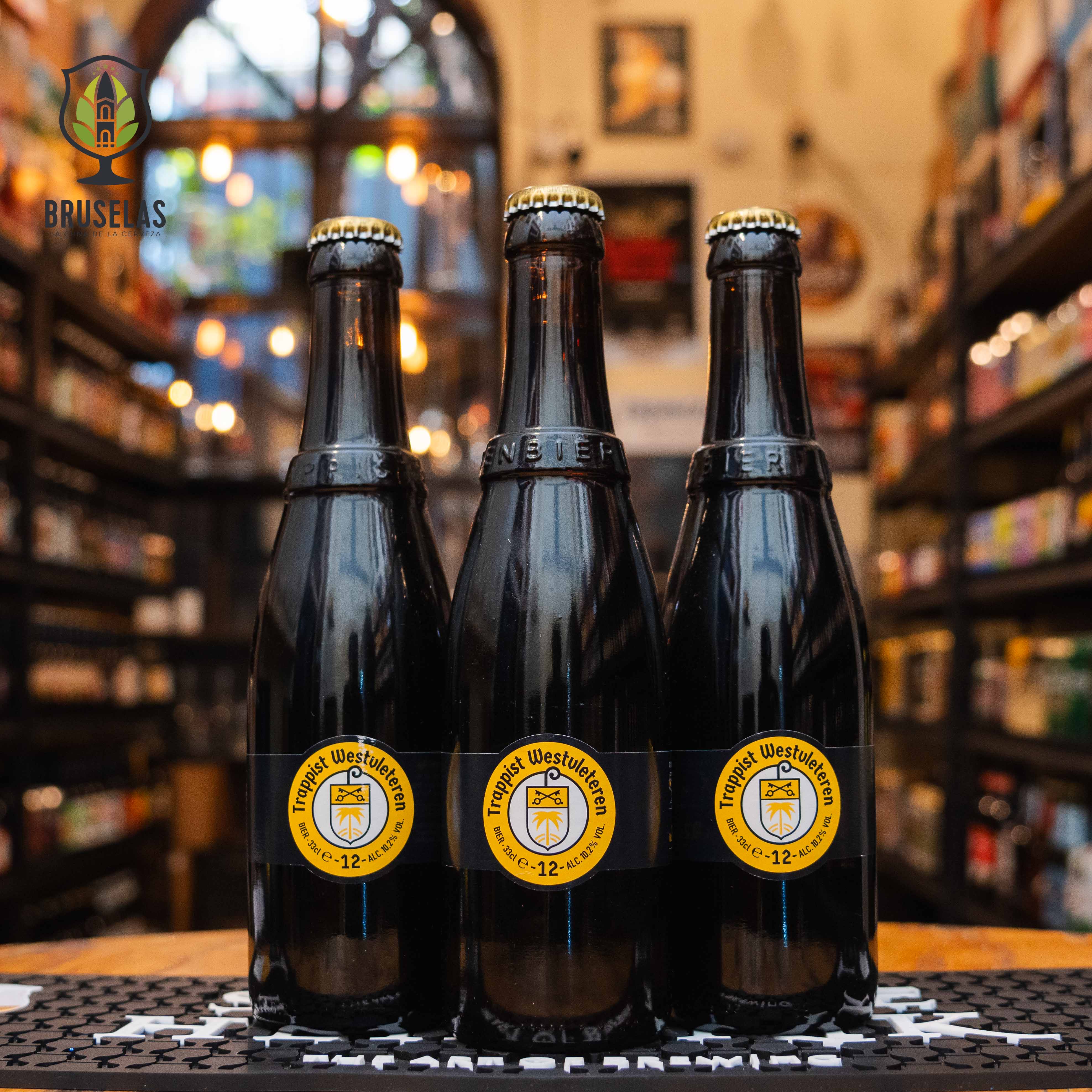 Botella de Westvleteren XII, una cerveza trapense belga de estilo Quadrupel. La etiqueta es un simple anillo negro con un logo amarillo. ABV de 10.2%. Sabor complejo con notas de frutas oscuras, caramelo, malta tostada y especias. Ideal para acompañar quesos fuertes, carnes asadas y postres de chocolate. Famosa por su exclusividad y considerada una de las mejores cervezas del mundo.