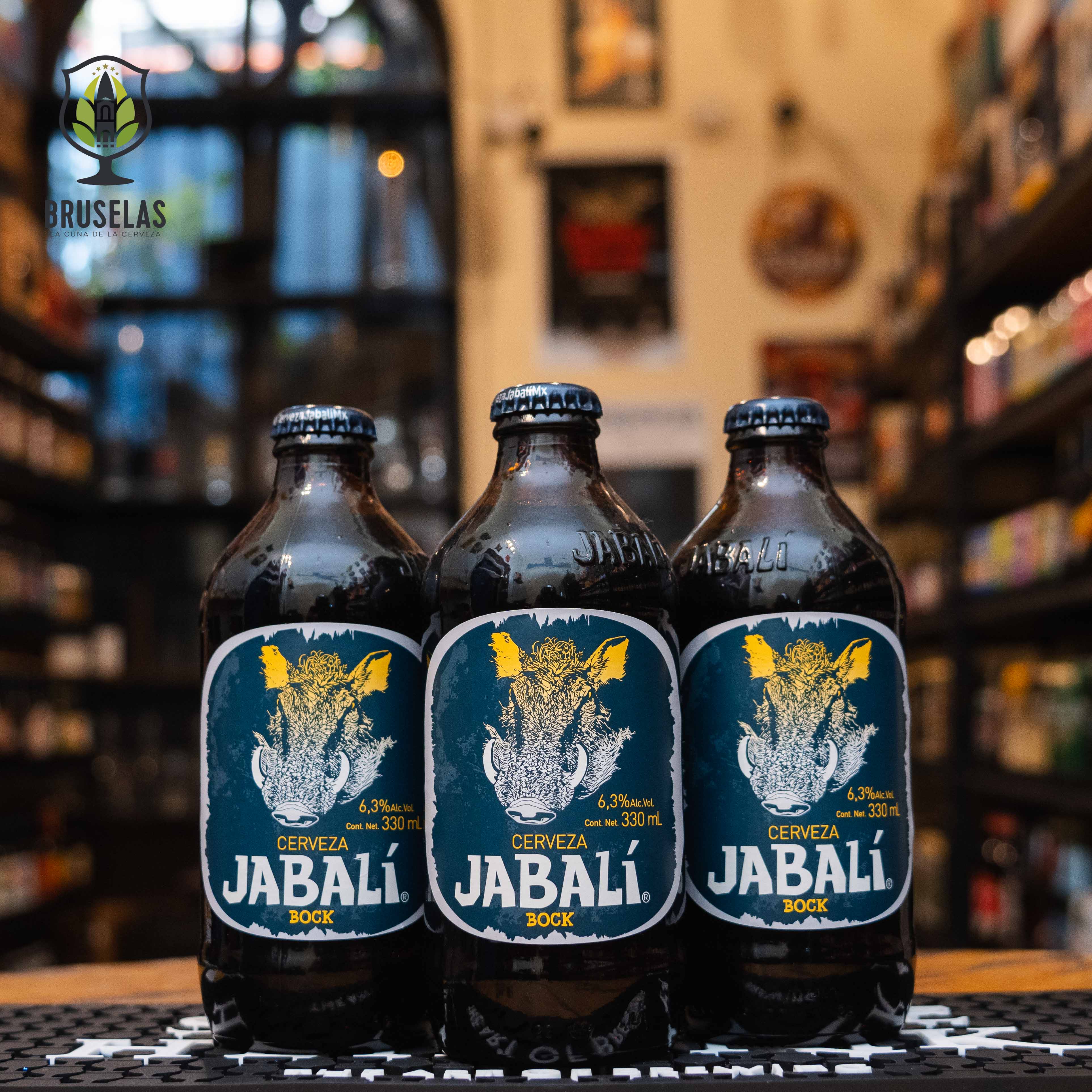 Botella de Jabalí Bock, una cerveza artesanal de estilo Bock elaborada en México con un ABV de 6.3%. La etiqueta muestra la ilustración de un jabalí en tonos blancos y dorados sobre un fondo azul oscuro. Esta cerveza ofrece aromas de maltas tostadas, caramelo y chocolate, con un sabor dulce y un final ligeramente amargo. Ideal para acompañar carnes rojas, quesos fuertes y postres de chocolate. Presentación en botella de 330 ml