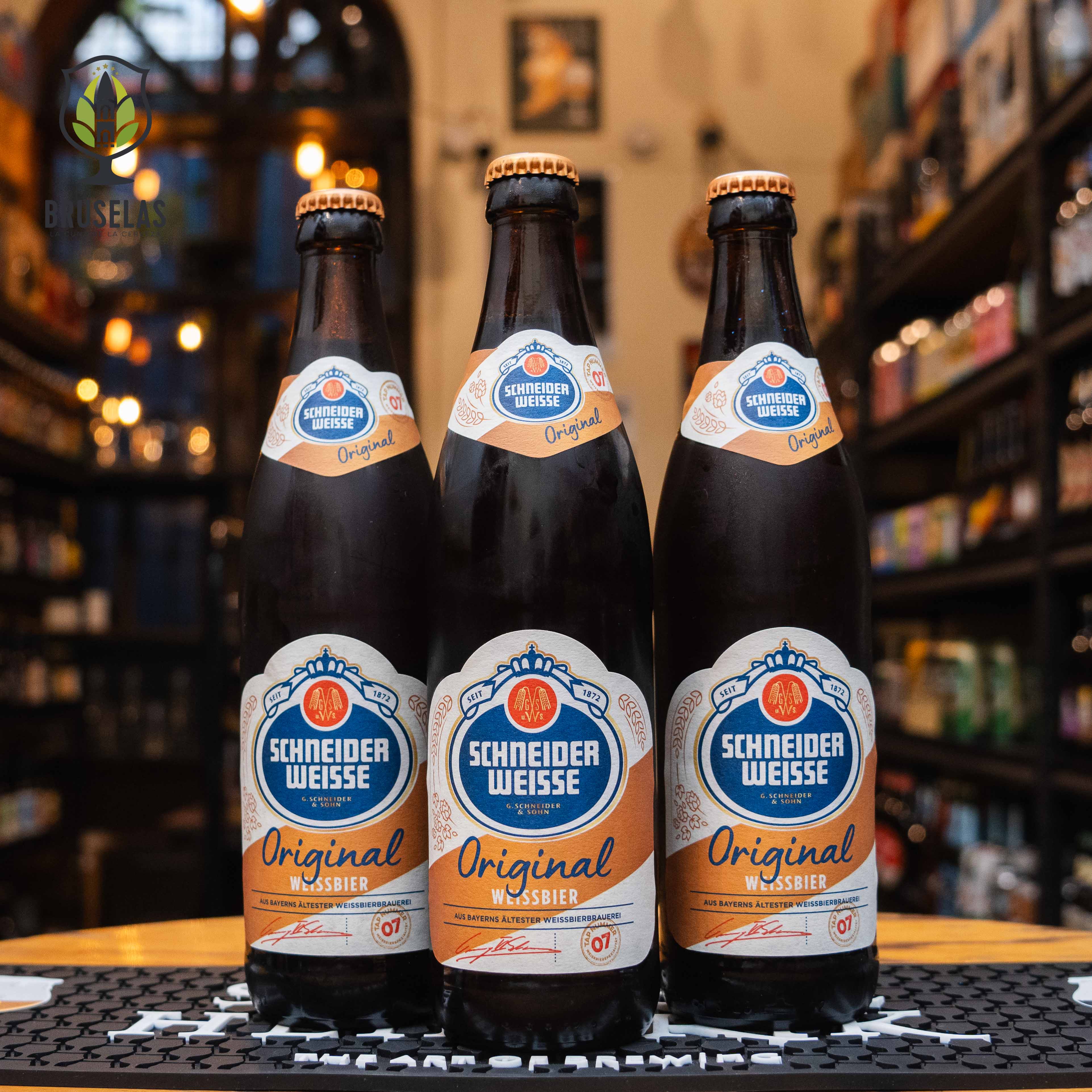 Botella de Schneider Weisse TAP 7 'Mein Original', una Weissbier alemana de Schneider Weisse G. Schneider & Sohn. La etiqueta es azul y blanca con detalles anaranjados. ABV de 5.4%, con aromas de plátano, clavo y caramelo. Sabor equilibrado entre dulzor frutal y especias, con un final refrescante. Ideal para acompañar salchichas alemanas, carnes asadas y pretzels. Diseño tradicional.