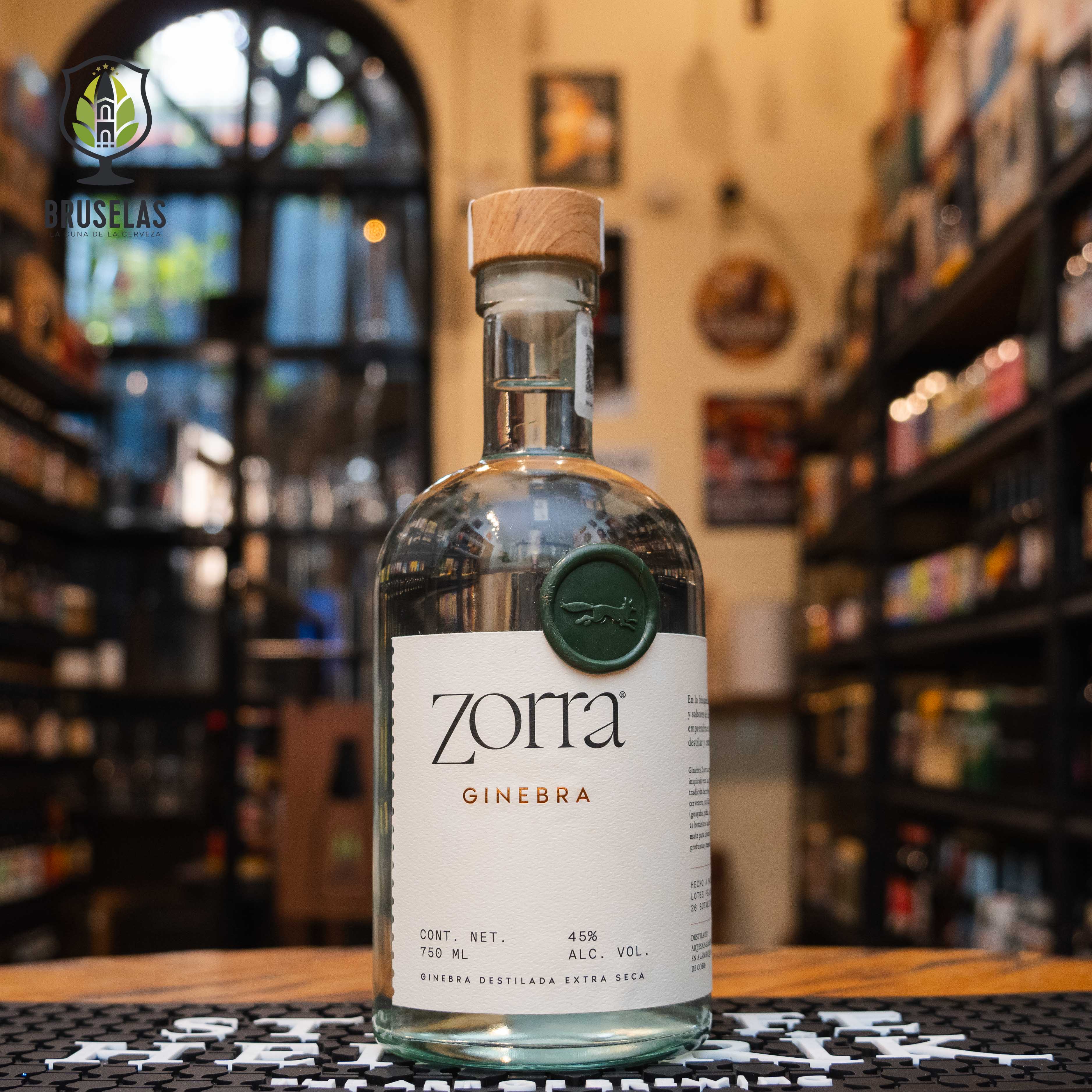 Botella de Ginebra Zorra, un destilado artesanal con un ABV de 45%. La etiqueta es minimalista con detalles verdes y tapa de madera. Esta ginebra se elabora con 26 botánicos, incluyendo guayaba, mango, piña, enebro y lúpulo. Sabor fresco, afrutado y con toques herbales. Ideal para cócteles o disfrutar sola. Presentación en botella de 750 ml.