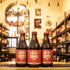 Botella de Chimay Rouge, también conocida como Chimay Première, una Dubbel belga de la Abbaye de Scourmont. Con un ABV de 7%, esta cerveza presenta un color cobre oscuro y espuma cremosa. Ofrece aromas de frutas oscuras como albaricoque y cereza, con especias y toques de caramelo. Su sabor equilibra dulzor y amargor, con notas de frutas, caramelo y un toque de regaliz. Ideal para acompañar carnes asadas, quesos suaves y postres de frutas.