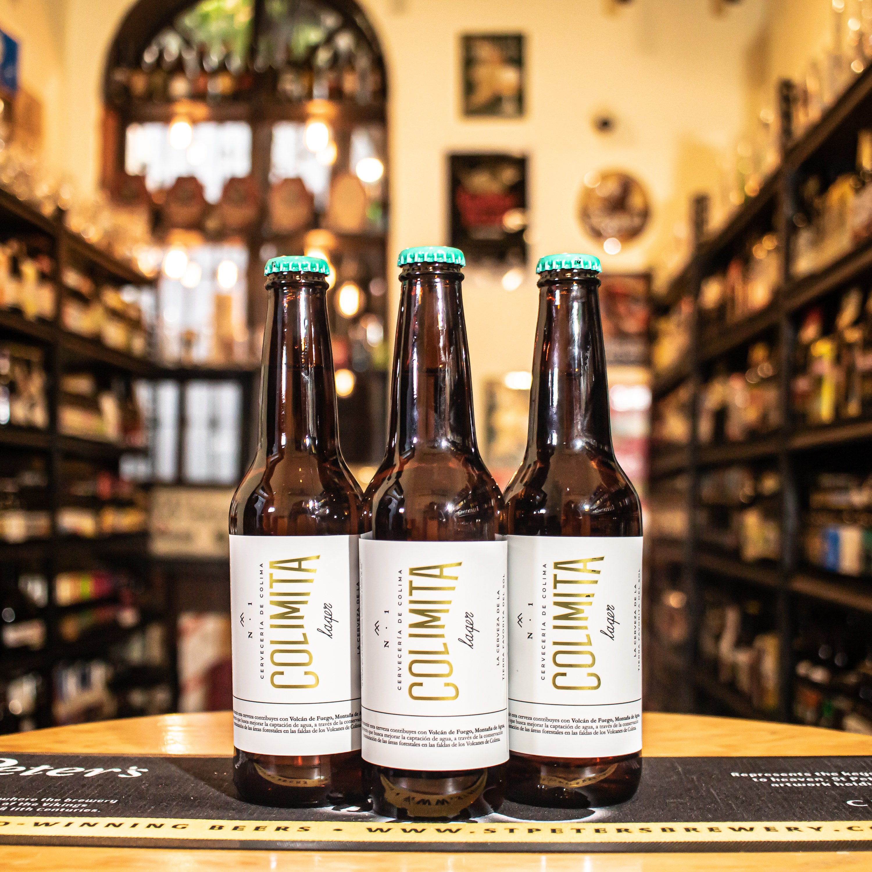 Botella de Colimita Lager, una lager artesanal mexicana de la Cervecería de Colima. Inspirada en el estilo pilsner alemán, con un ABV de 4.4%, presenta un color pajizo y espuma fina. Su aroma incluye notas florales y lúpulo fresco, mientras que su sabor es equilibrado con un ligero amargor y un toque floral. Ideal para maridar con mariscos, ensaladas frescas y platos ligeros.