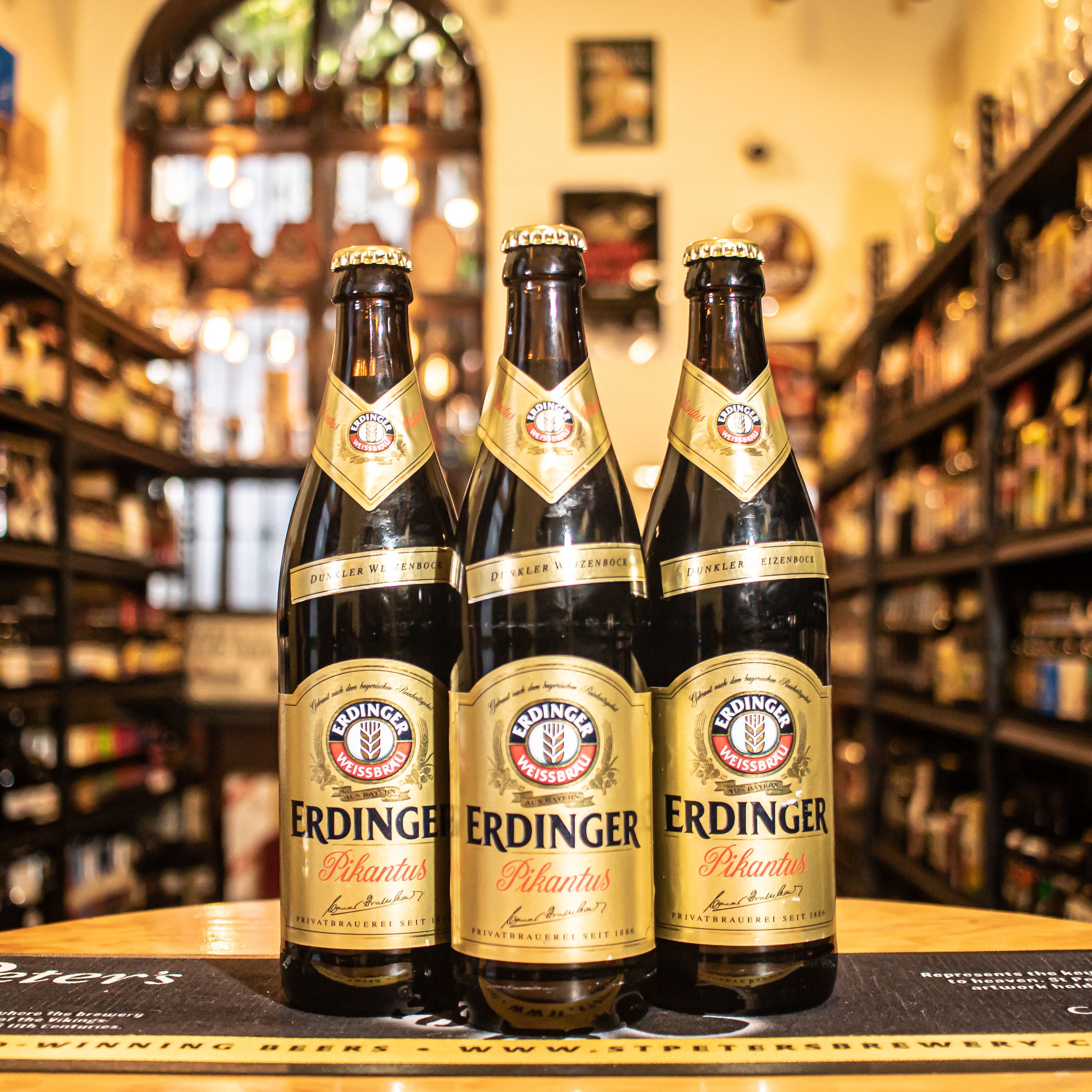 Botella de Erdinger Pikantus, una Weizendoppelbock elaborada por Erdinger Weissbräu. Con un ABV de 7.3%, es la cerveza más fuerte de la gama Erdinger, destacando por su color marrón oscuro y espuma cremosa beige. Ofrece aromas especiados como clavo, junto con notas de frutos rojos, chocolate y regaliz. En boca, presenta sabores intensos con nuez moscada y un final sedoso. Ideal para maridar con cerdo asado, jamón ahumado y quesos maduros. Presentación en botella de 500 ml.