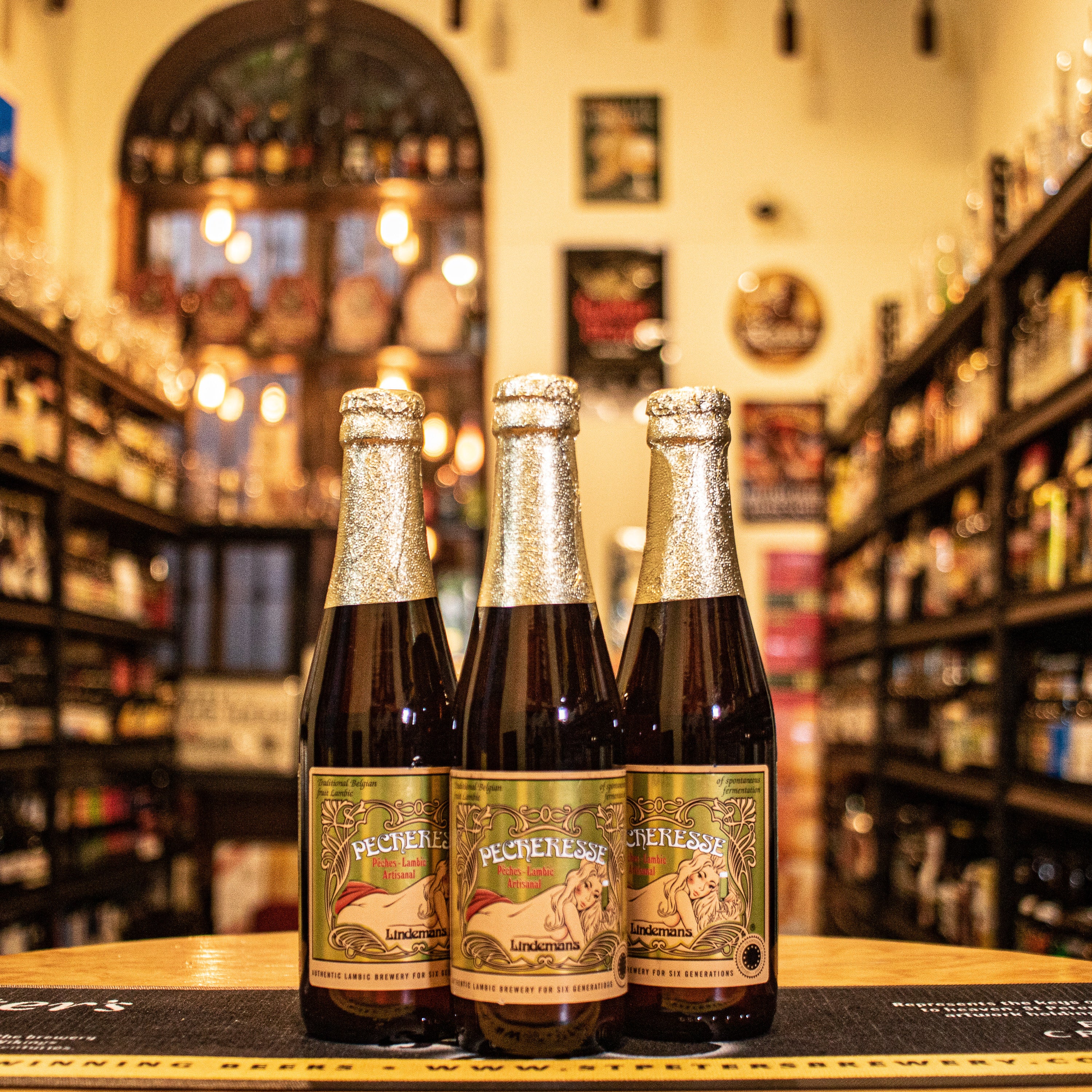 Botella de Lindemans Pecheresse, una Fruit Lambic belga de Brouwerij Lindemans. Con un ABV de 2.5%, está elaborada con jugo de durazno. Ofrece aromas de durazno maduro y un toque de acidez. Su sabor es dulce y ligeramente ácido, equilibrando el durazno con la acidez del lambic, con un final refrescante. Ideal para maridar con postres ligeros, ensaladas de frutas o como aperitivo refrescante.