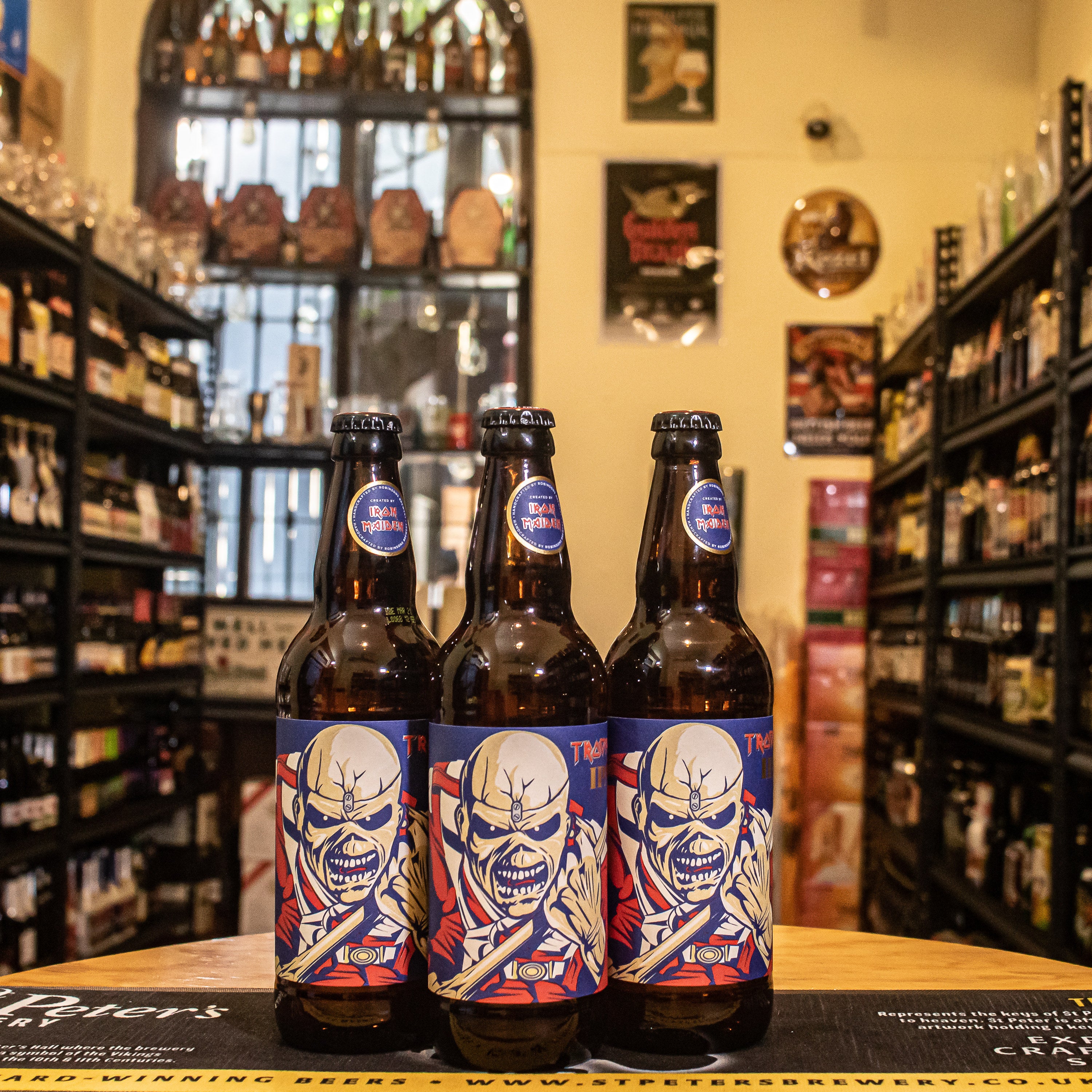 Botella de Trooper IPA, una India Pale Ale lanzada por Iron Maiden y Robinsons Brewery, con un ABV de 4.3%. Se caracteriza por su aroma floral, cítrico y tropical, con sabores a mango y toronja. Su amargor moderado equilibra la dulzura, brindando una experiencia refrescante y de cuerpo medio. Ideal para maridar con comidas especiadas, hamburguesas y platos de sabores intensos.