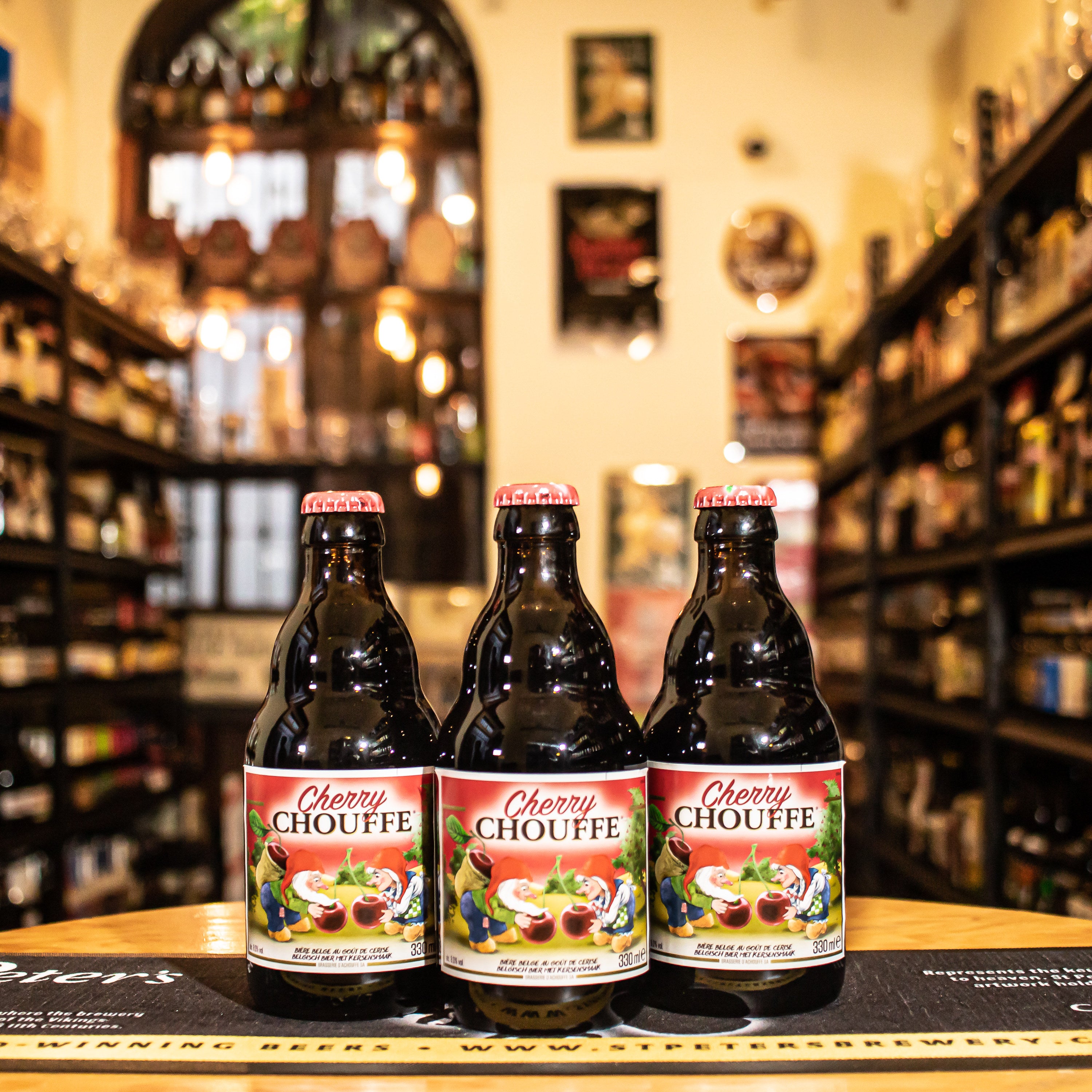 Botella de D'Achouffe Cherry Chouffe, una Fruit Beer belga de Brasserie d'Achouffe. Con un ABV de 8%, esta cerveza combina la dulzura y acidez de las cerezas con el carácter robusto de La Chouffe. Presenta aromas de cereza madura, especias como clavo y pimienta, y un toque maltoso. En boca, es vibrante, equilibrando dulzor y acidez con un final afrutado y ligeramente seco. Ideal para maridar con postres de chocolate, tartas de frutas y quesos fuertes. Presentación en botella de 330 ml.